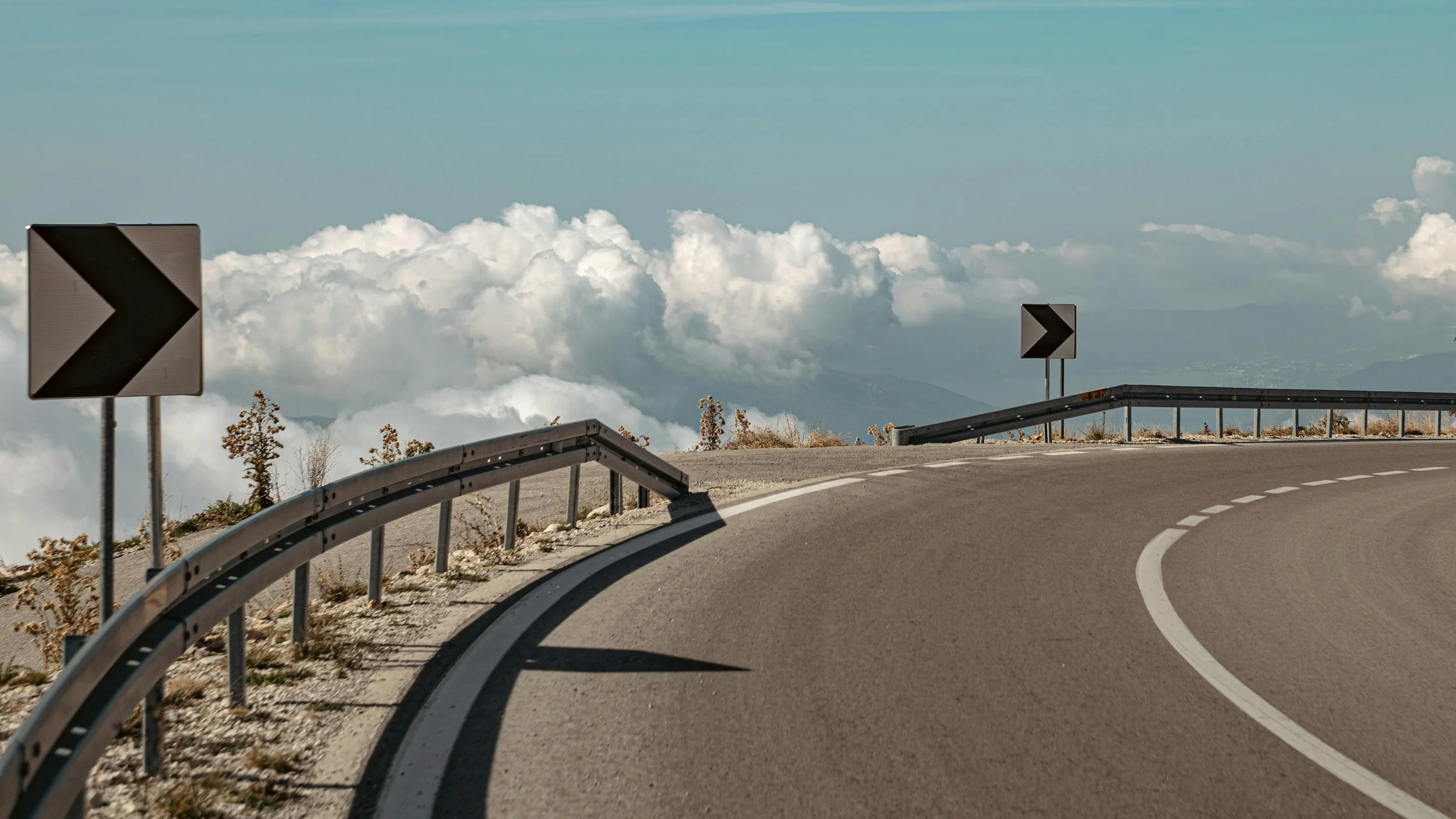 A winding mountain road with guardrails curving above the clouds, representing how strategic constraints keep product teams focused and moving in the right direction.
