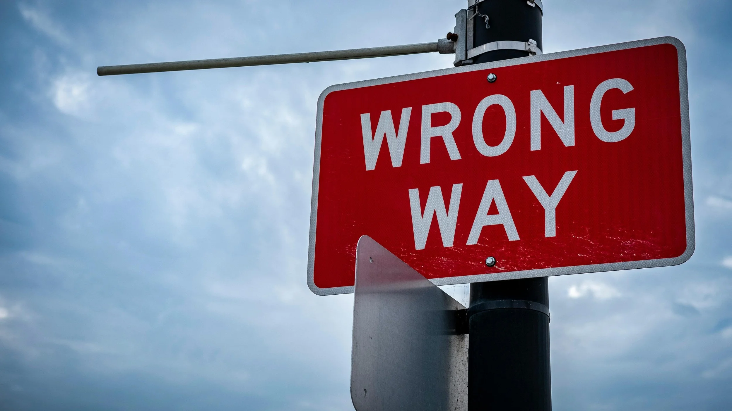 A close-up of a red wrong way road sign against a dark overcast sky, a visual warning that metrics don't always signal when they're driving behavior in the wrong direction.