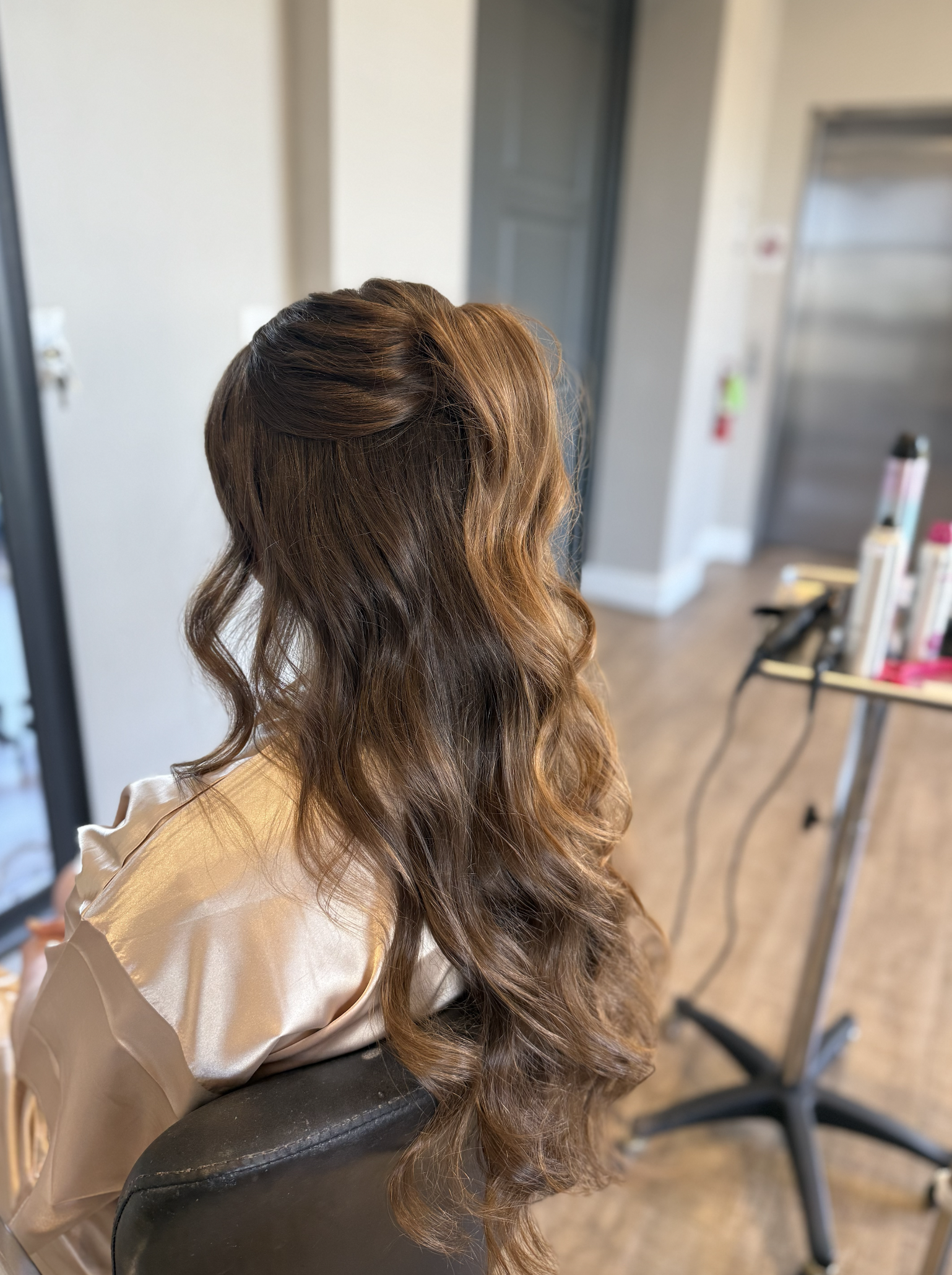 Side view of a woman with long, wavy, brown hair sitting in a salon chair.