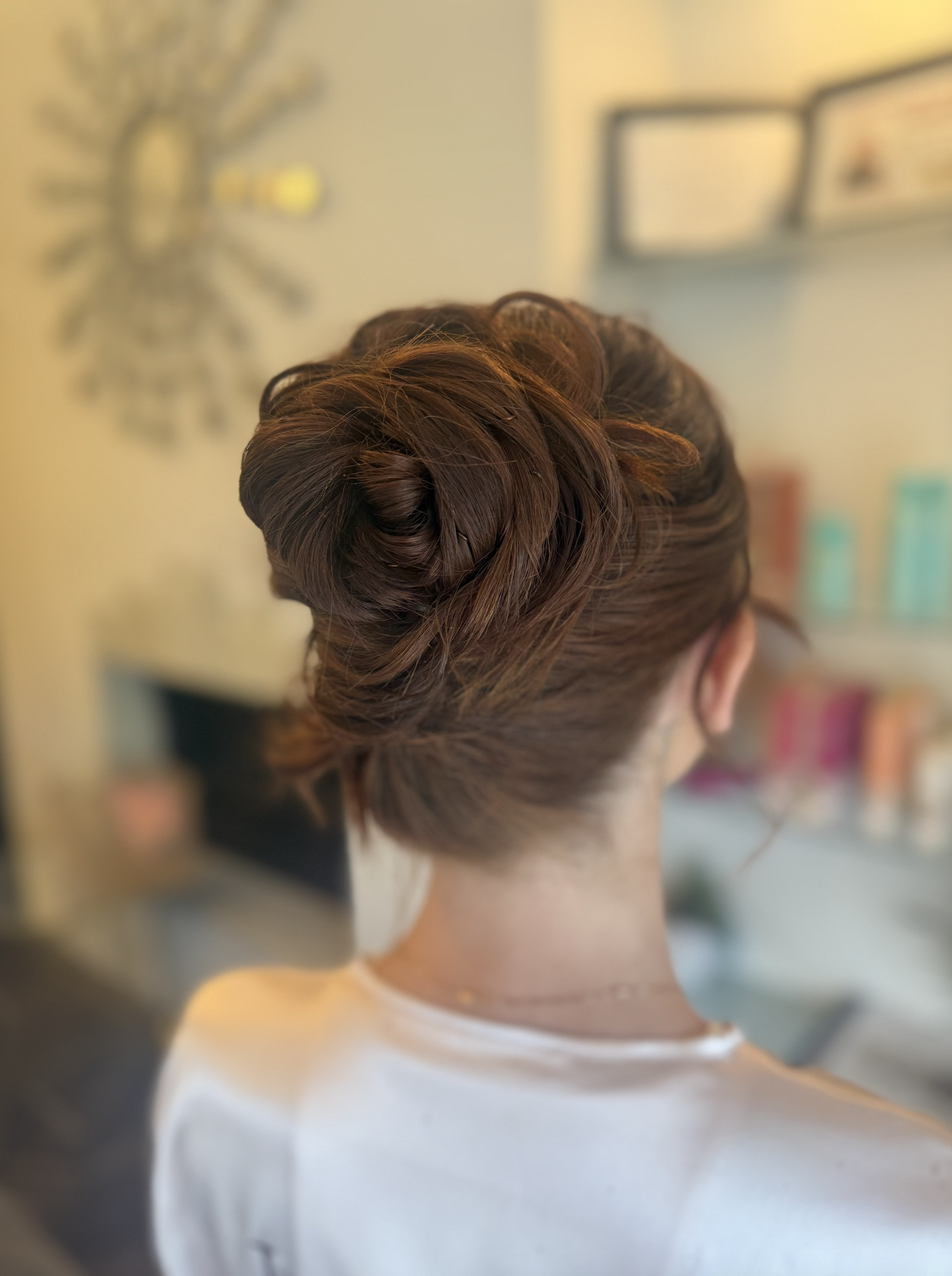 Back view of a woman with an elegant updo hairstyle, indoors with blurred background.