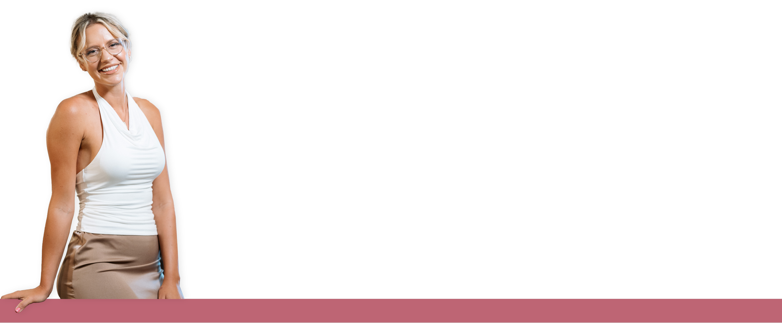 A woman with short blonde hair, glasses, wearing a white sleeveless top and beige skirt, smiling and leaning on a pink table.