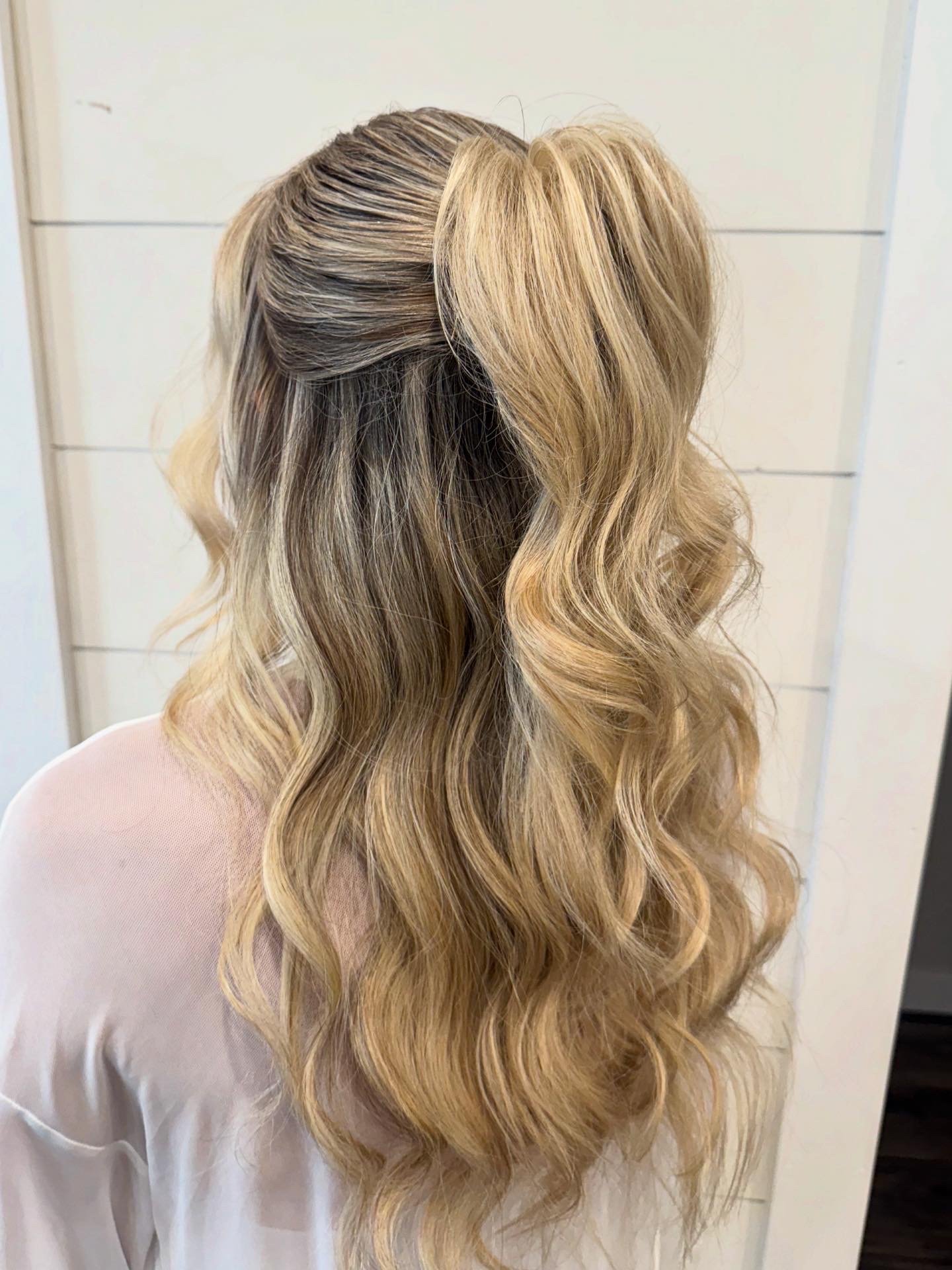 Back view of a woman with blonde hair styled in loose waves and a half-up, half-down hairstyle.