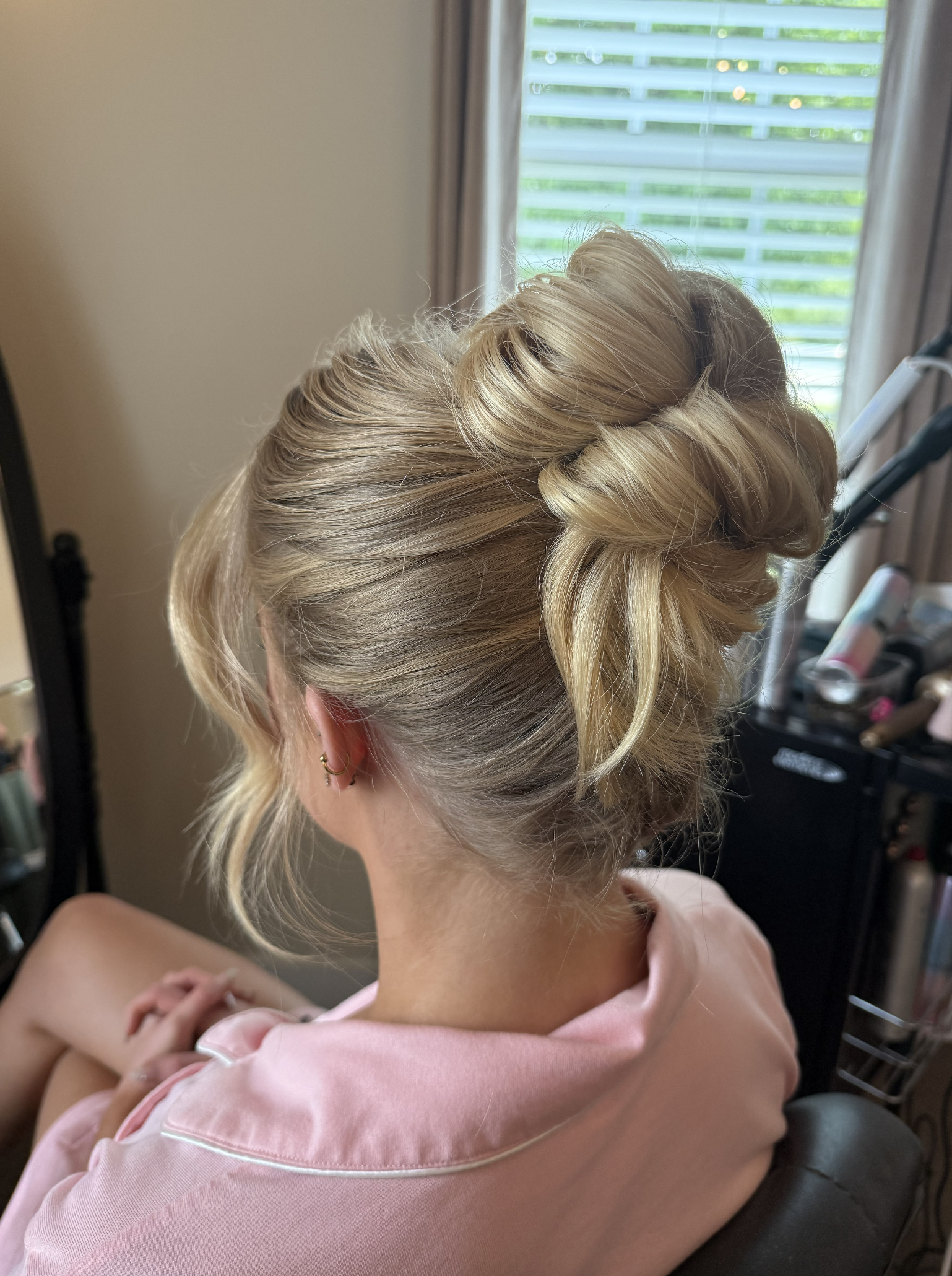 A woman with blonde hair in an elegant updo, sitting in a salon or dressing room.