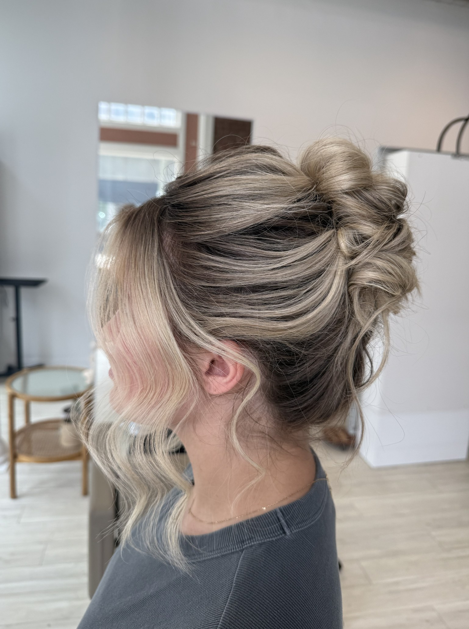Side view of a woman with styled blonde hair in an updo with loose curls and waves.
