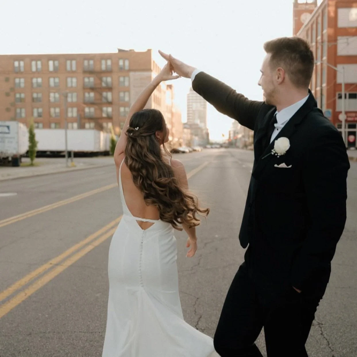 A bride and groom dancing on an empty city street during sunset, with the bride in a white gown and the groom in a black tuxedo.