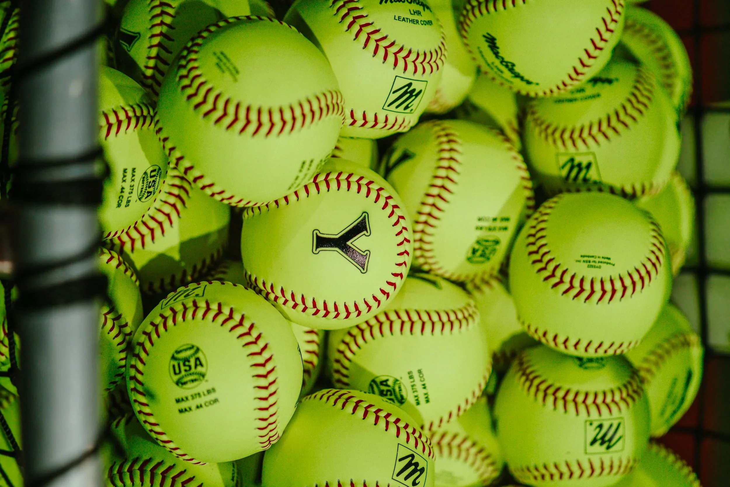 A pile of bright yellow baseballs with red stitching in a bin or display. The "Y" is a logo for The Yard Training. This facility is located in Anderson, SC.