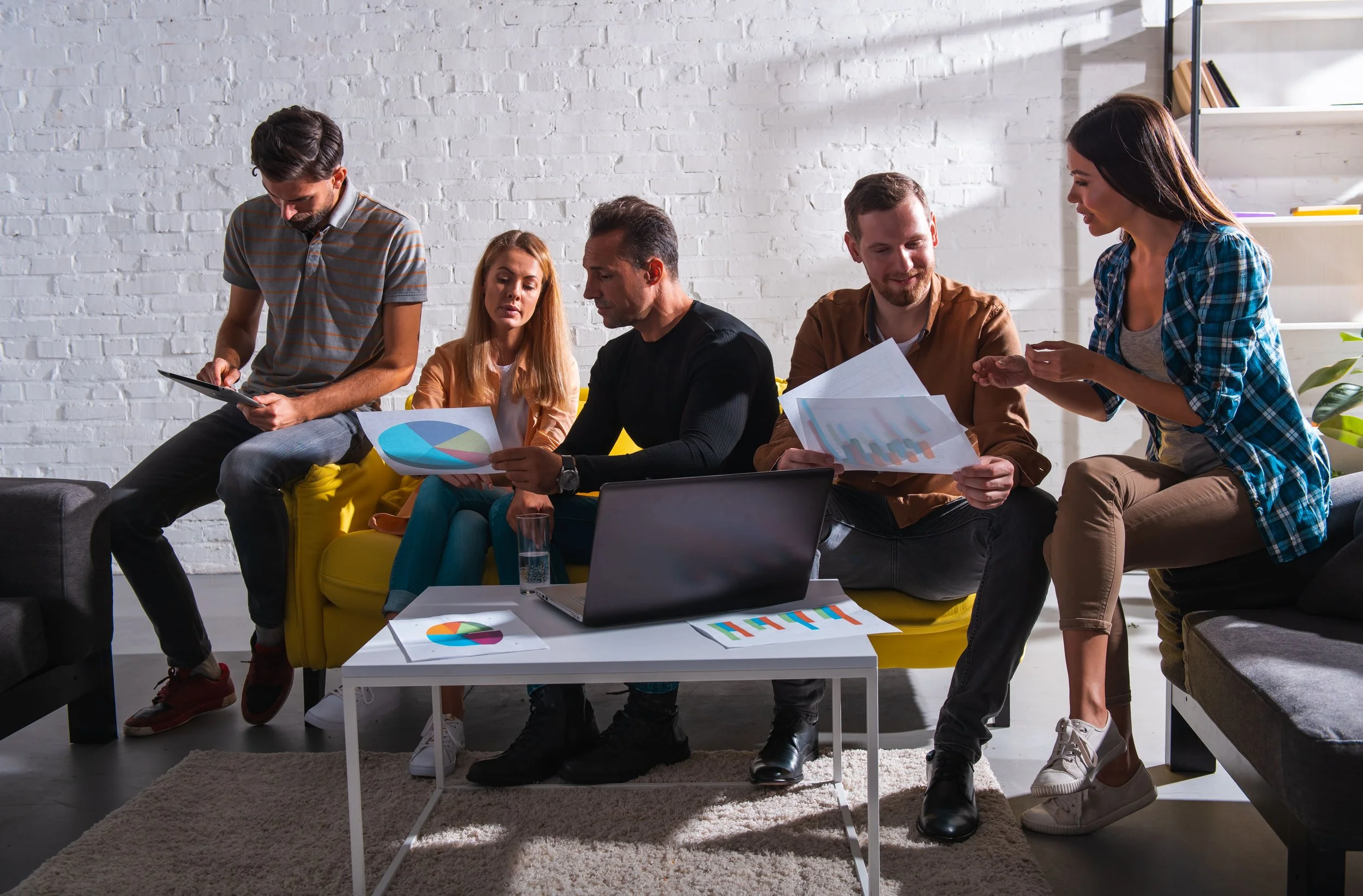 Group of five people working together in a modern office, discussing charts and data.