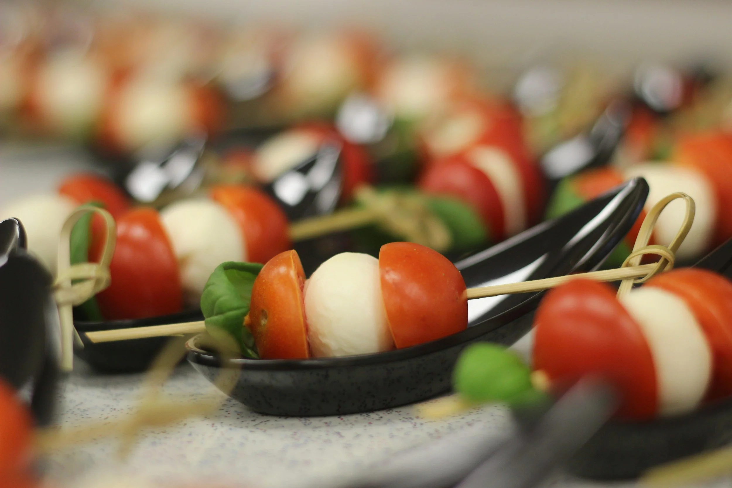 Skewers with cherry tomatoes, small mozzarella balls, and fresh basil leaves on black serving trays.