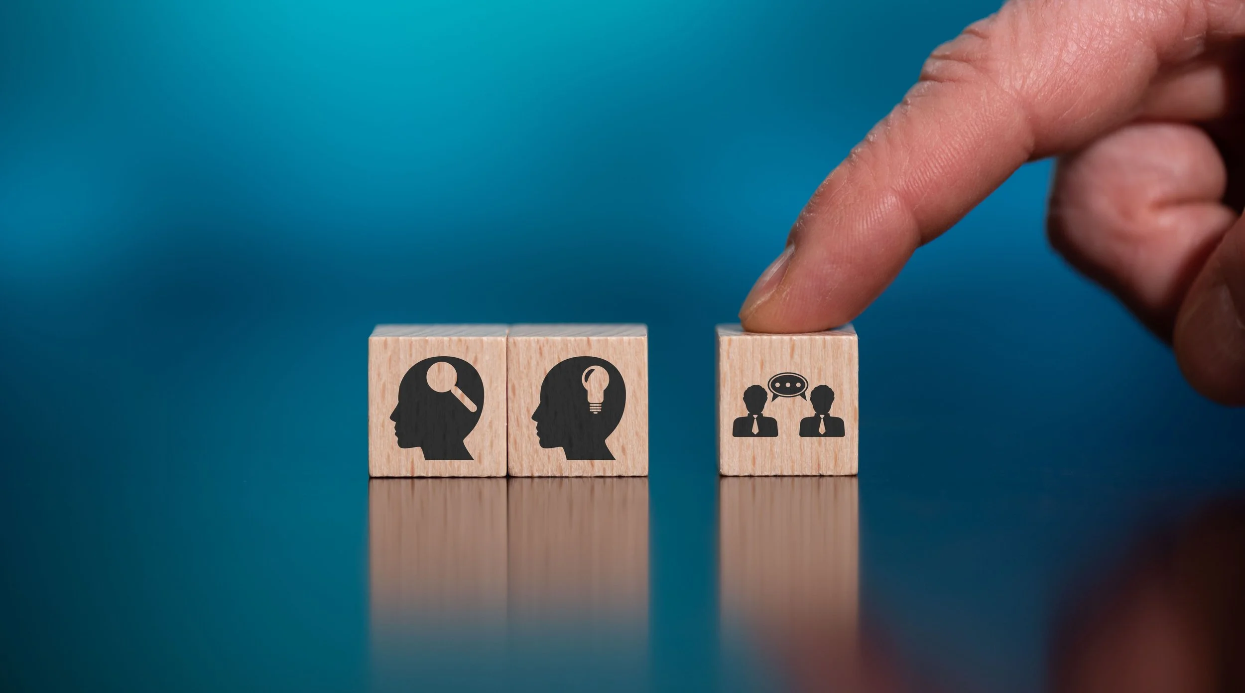 Three wooden blocks with icons, a hand is pressing the third block, which has a speech bubble icon with two people, representing communication.