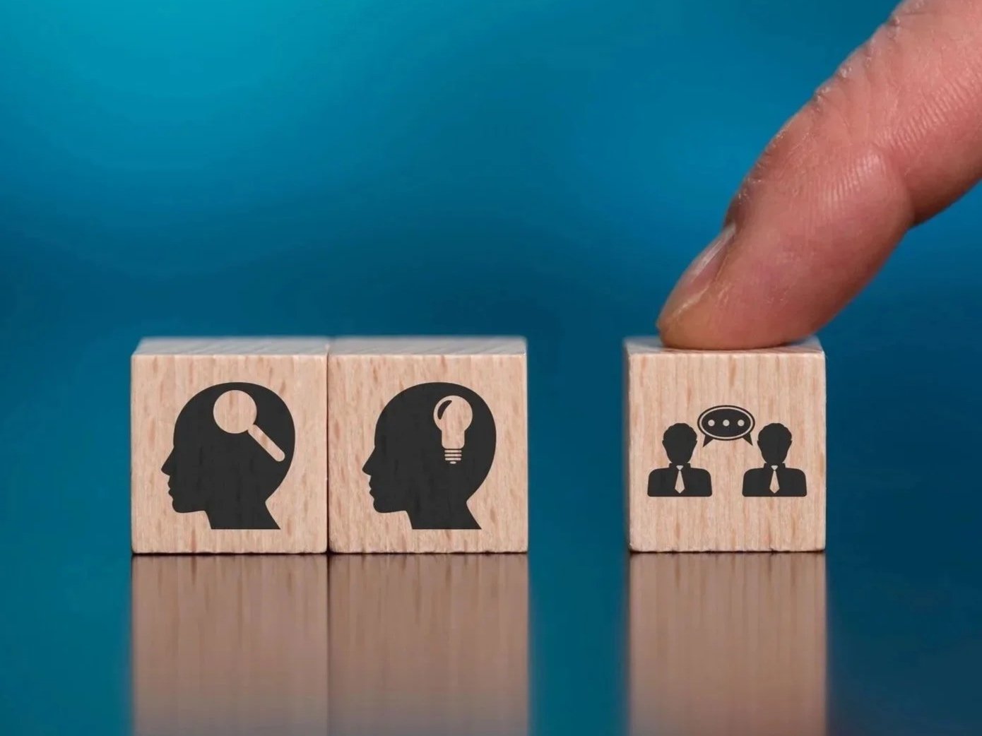 Three wooden blocks with icons: a human head with a magnifying glass, a human head with a light bulb, and two people with a speech bubble.