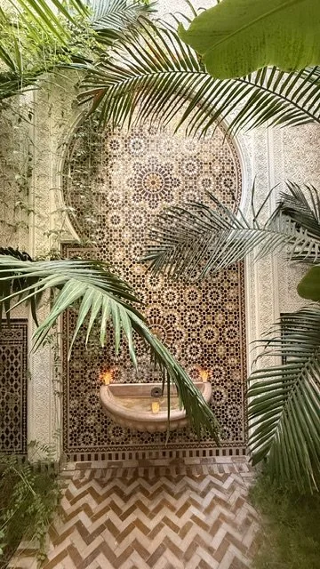 Moroccan riad courtyard wtih mosaic tilework, fountain and palm greenery