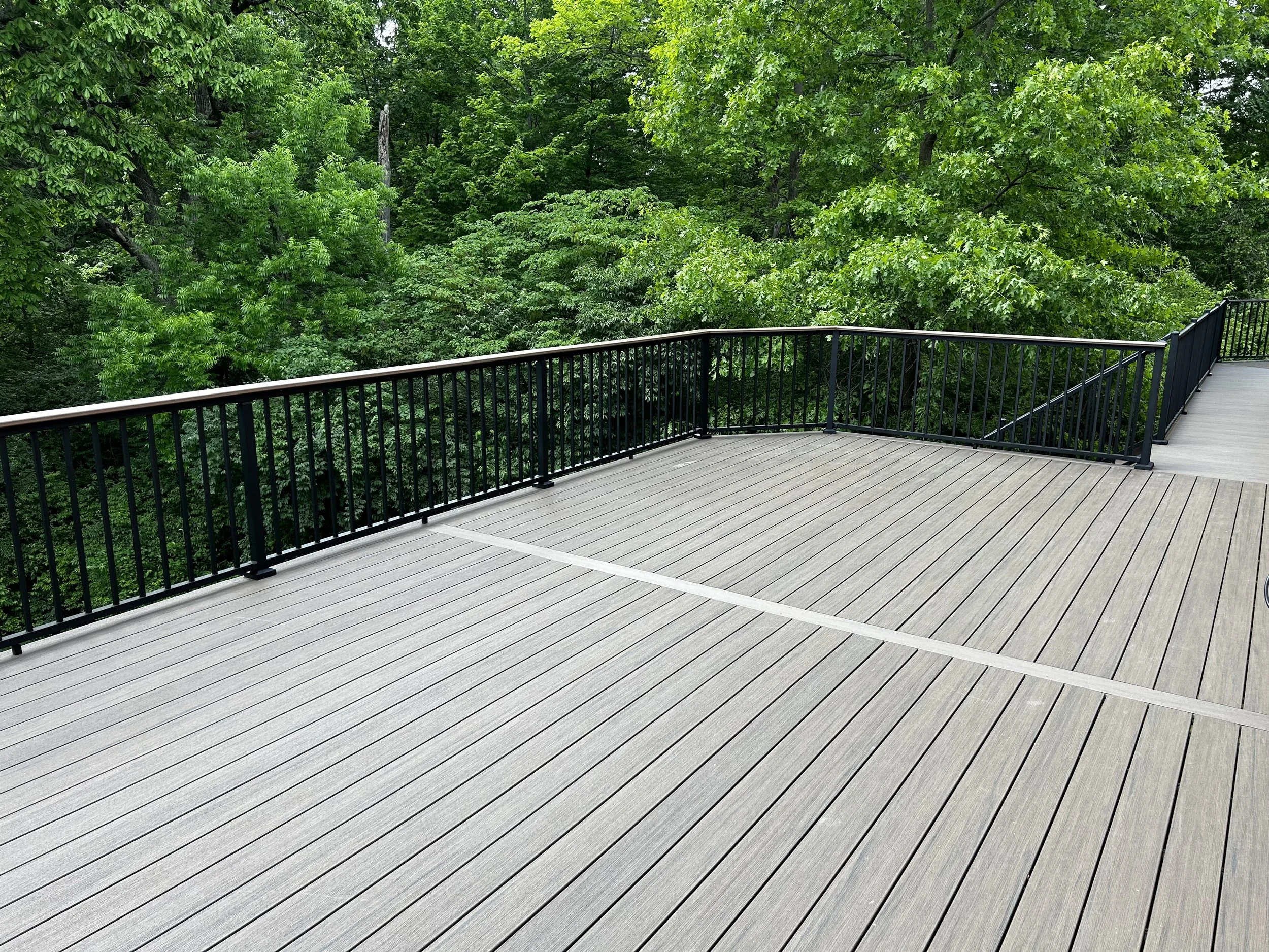 Composite deck with black metal railing overlooking dense green trees.