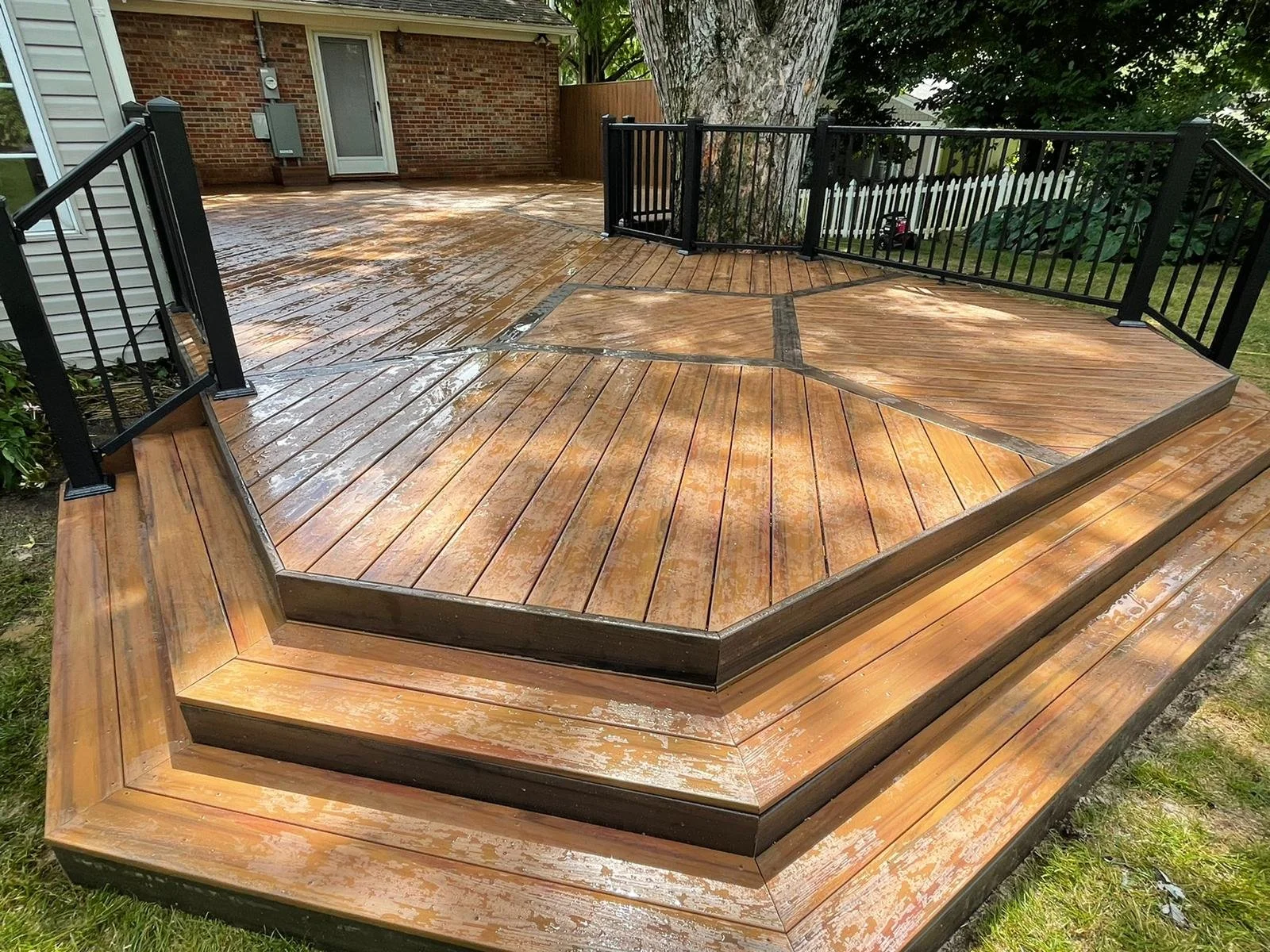 Custom hexagon composite deck with black aluminum railings built around a tree