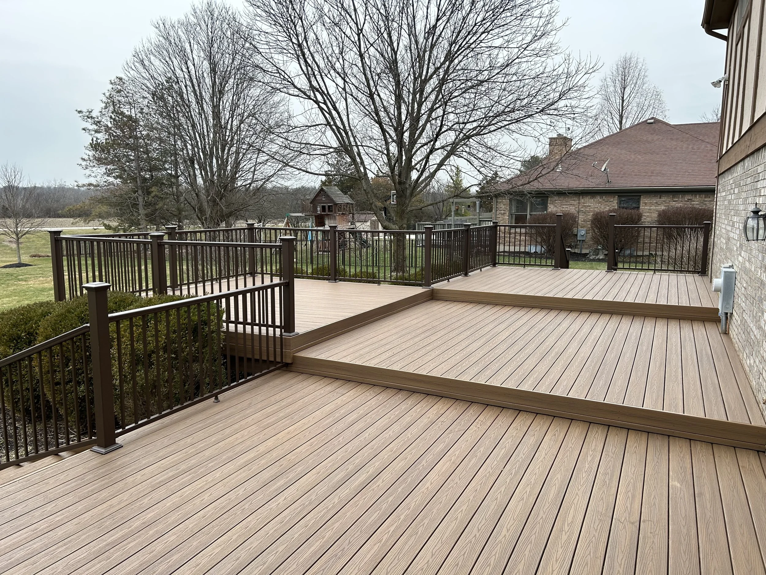 Multi-level composite deck with brown railings attached to a brick home in Ohio