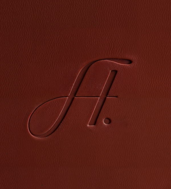 Close-up of a red leather surface with an embossed cursive letter 'J' and a period.