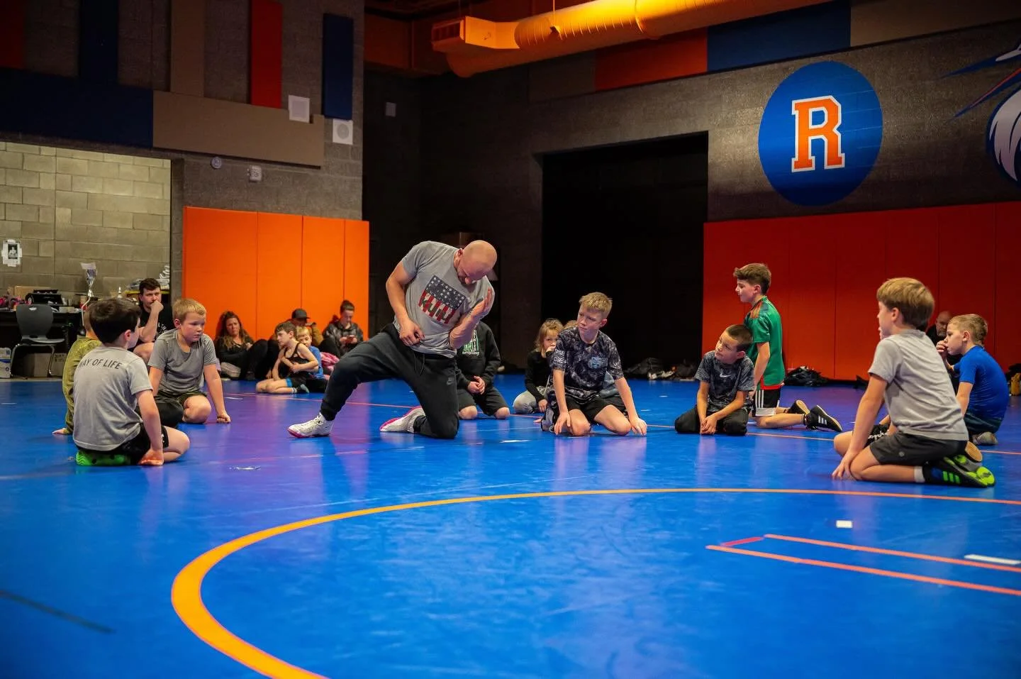 Youth wrestling coach leading summer practice with young athletes on wrestling mats during offseason training and development