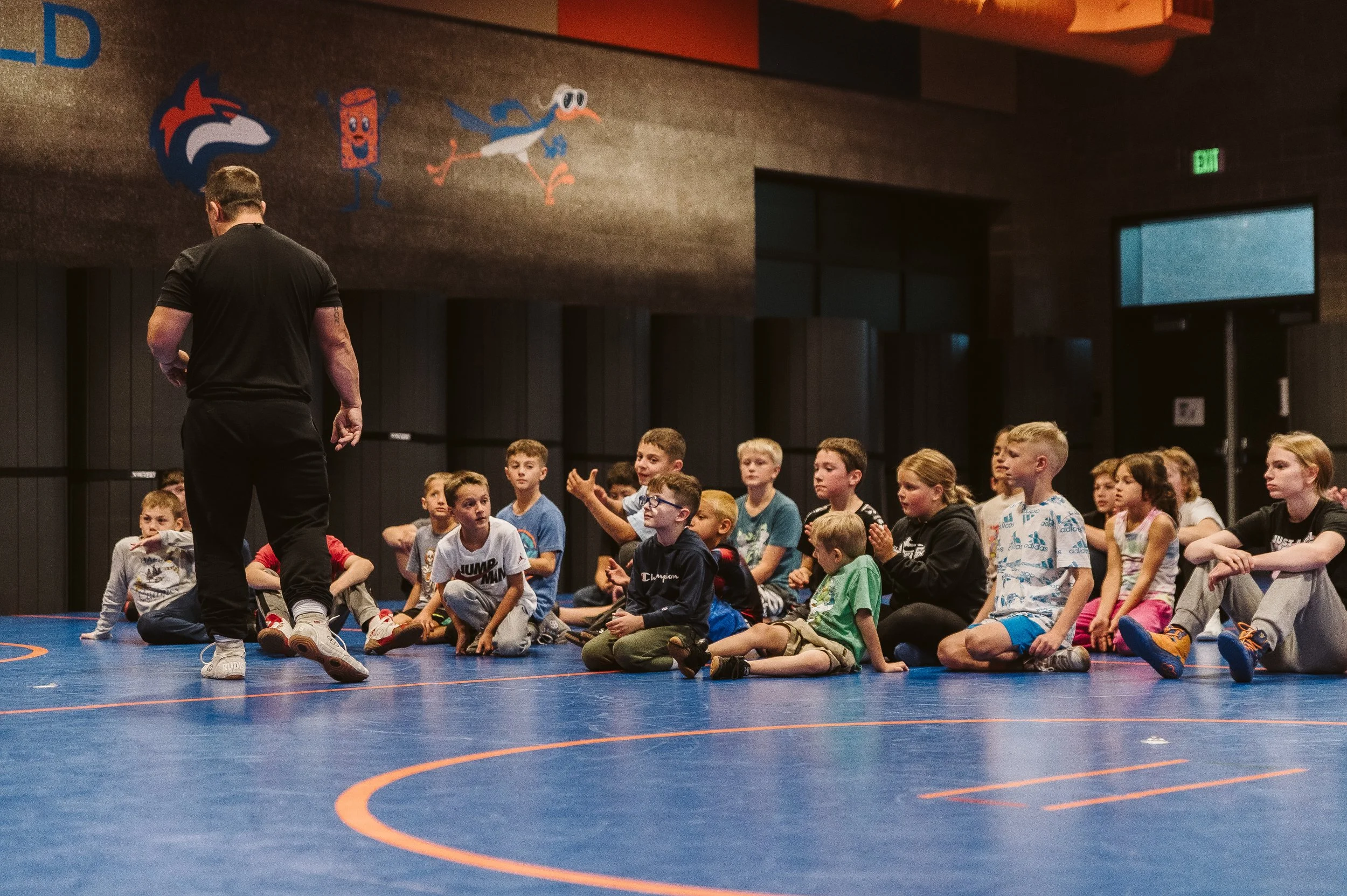 Youth wrestling coach leading a group of young athletes during practice, focused on long-term athletic development.