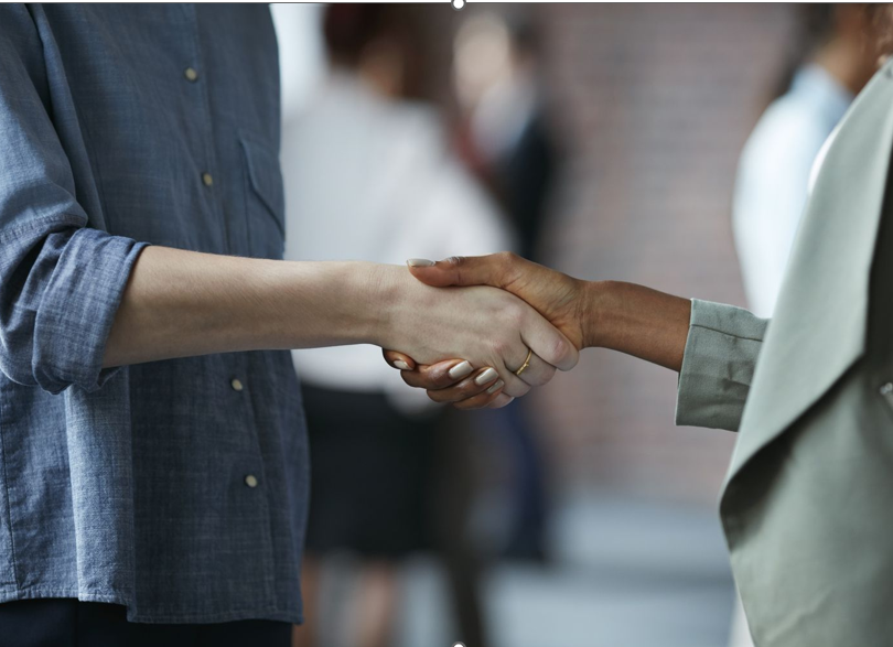 Two people shaking hands outdoors at a social or professional event.