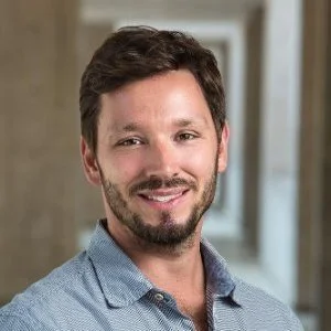 Portrait of Daniel B. Stern with dark hair and a beard, wearing a light blue shirt, standing in an indoor setting with natural light.