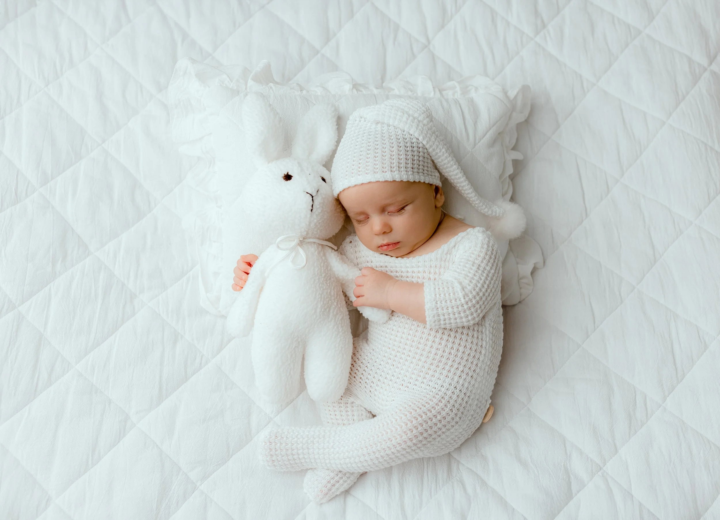 Sleeping newborn baby in a white knit outfit beside a stuffed bunny