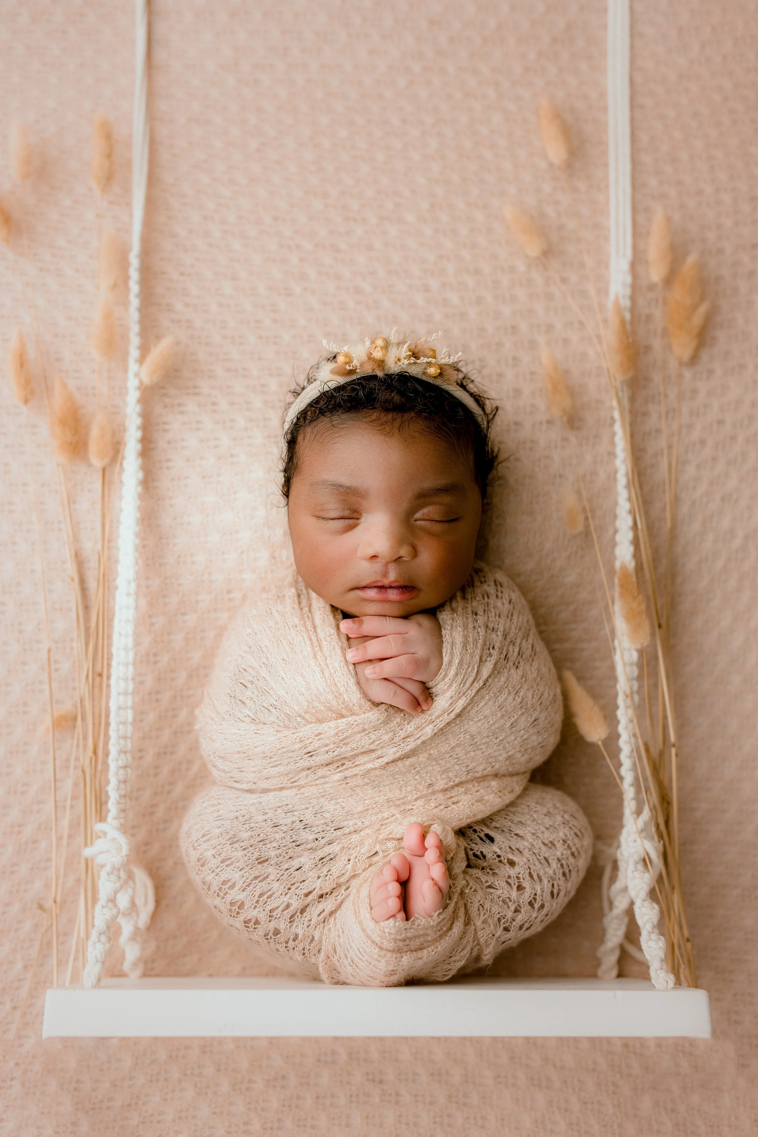 Newborn baby wrapped in blush pink posed on a miniature swing