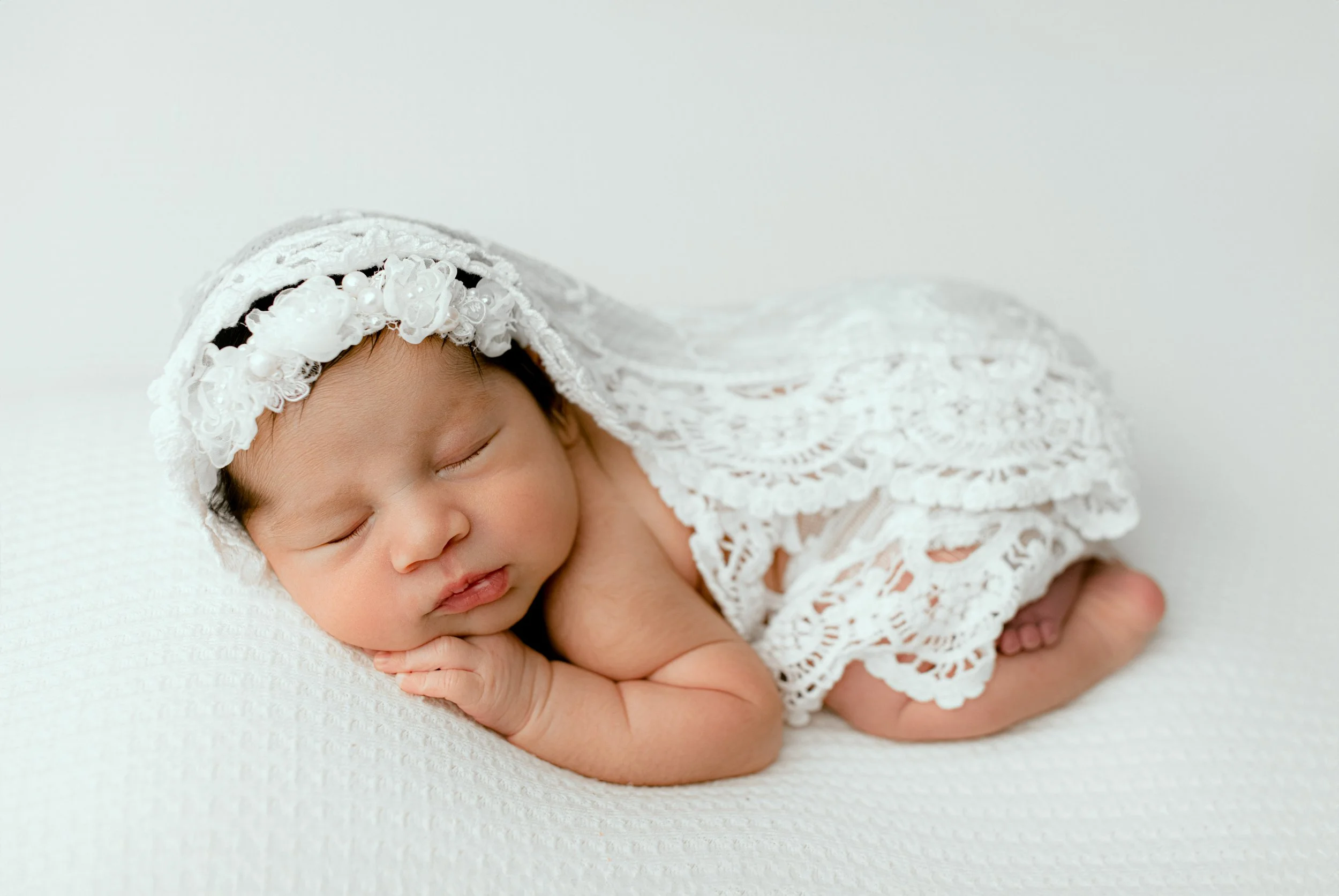 Sleeping newborn baby in a white lace wrap photographed in a Bonney Lake studio
