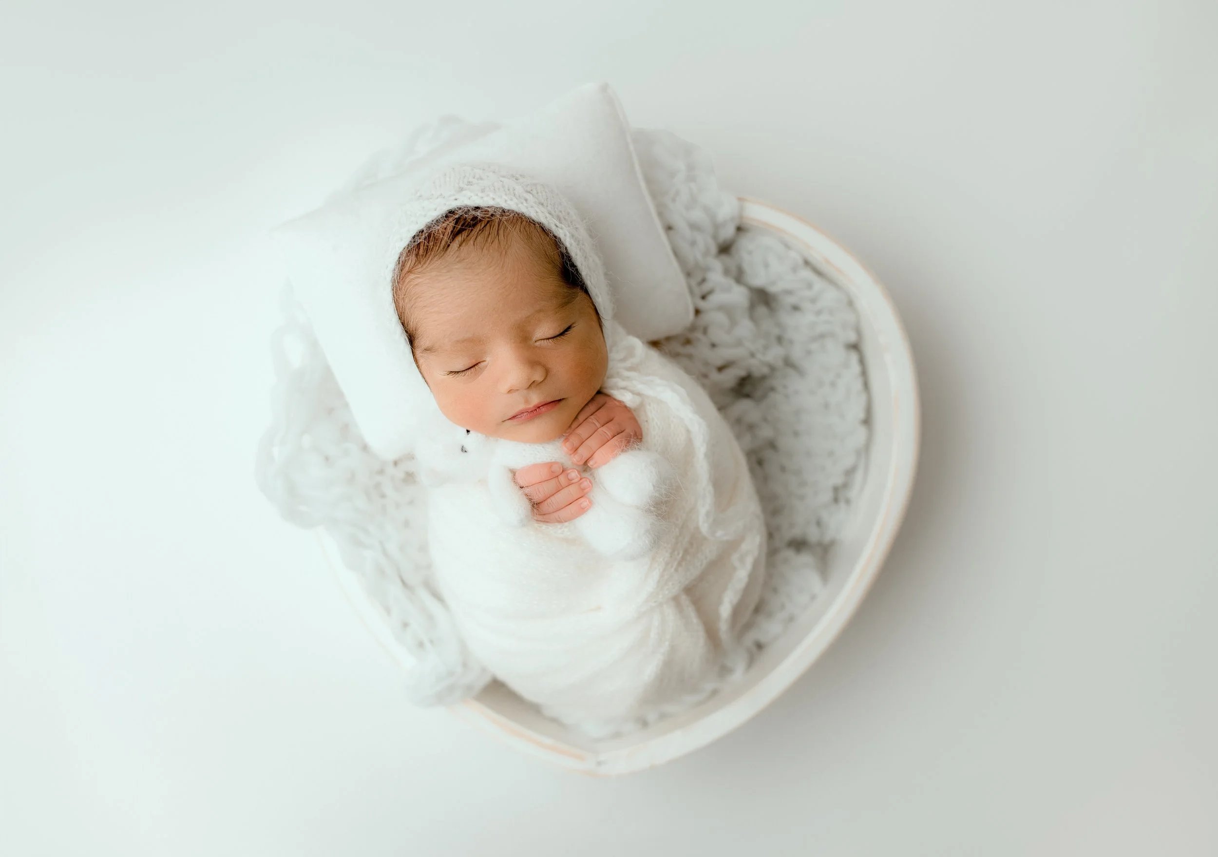 Sleeping newborn baby wrapped in white in a heart shaped white prop