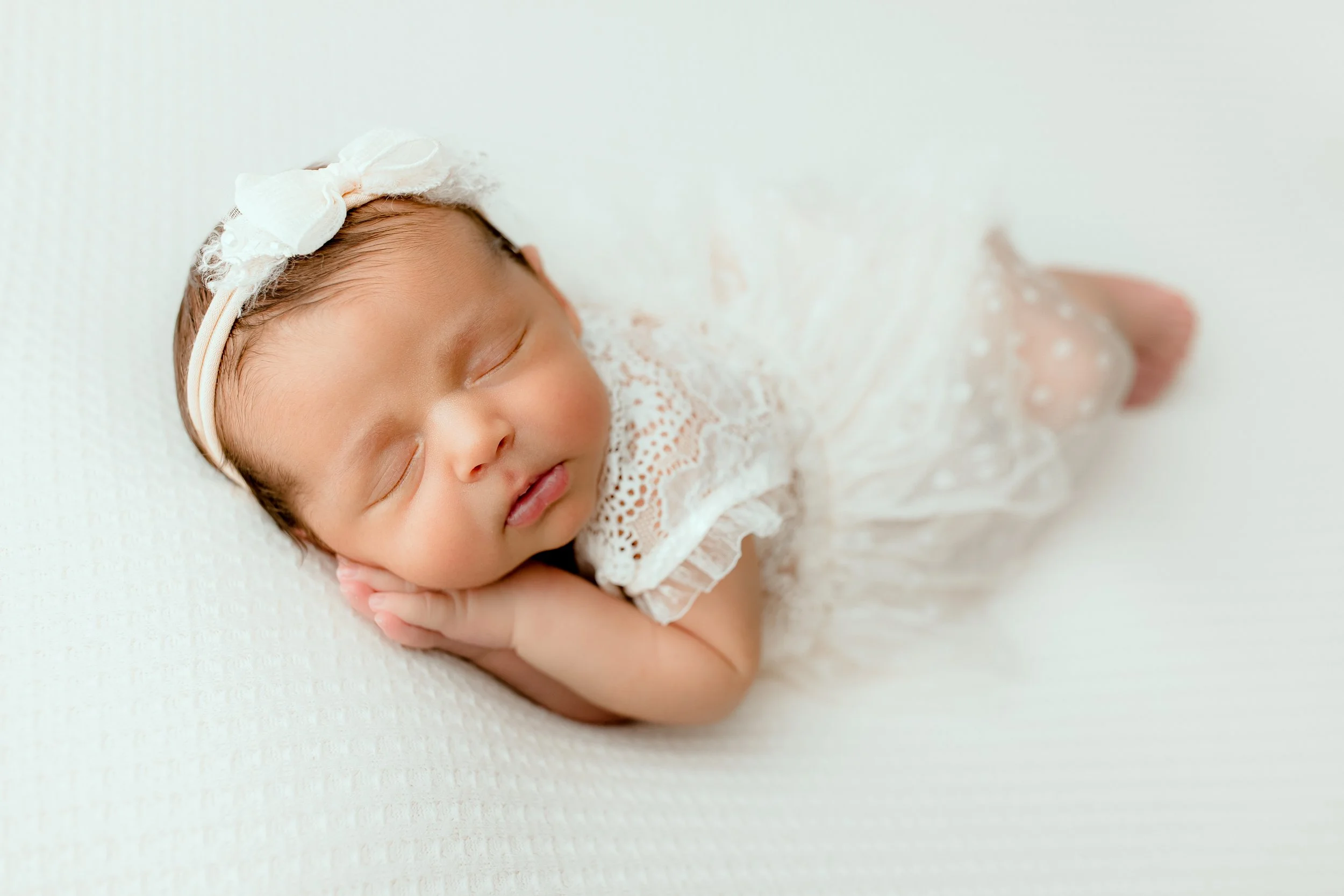 Close-up portrait of a sleeping newborn girl in soft white styling
