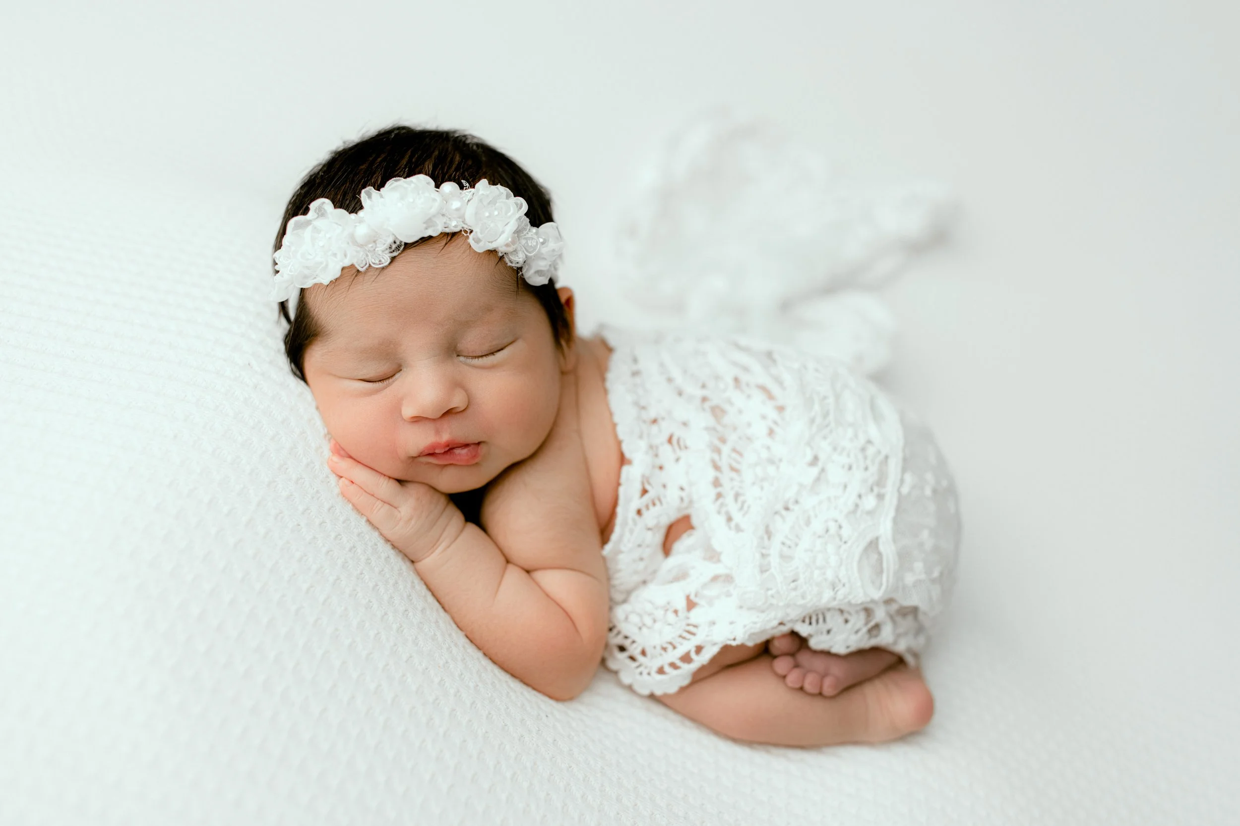 Sleeping newborn girl in a white lace wrap and floral headband