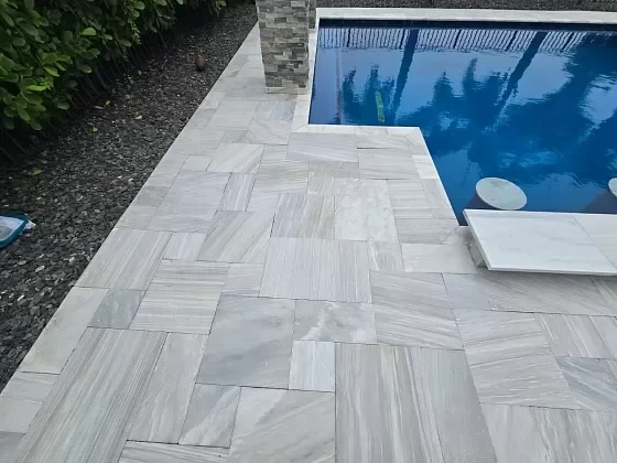 View of a swimming pool with a white tiled pool deck and a small white diving board.