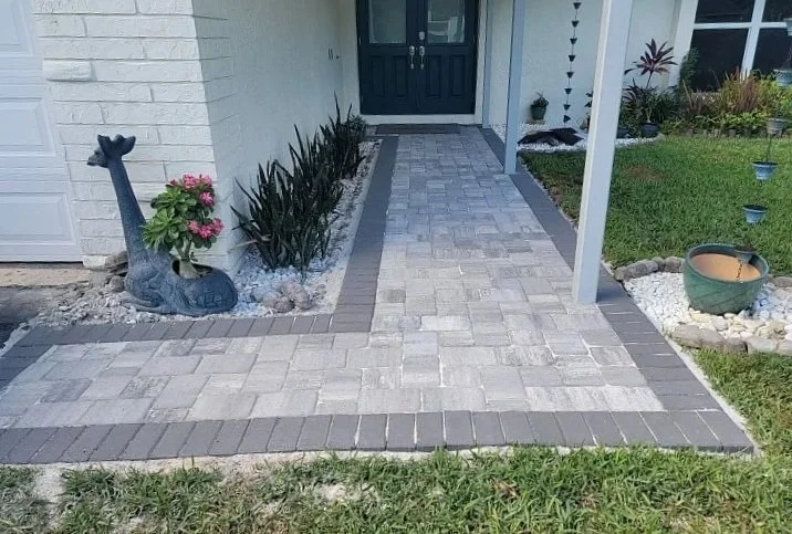 Paved walkway leading to a front door, with decorative plants and garden ornaments on both sides