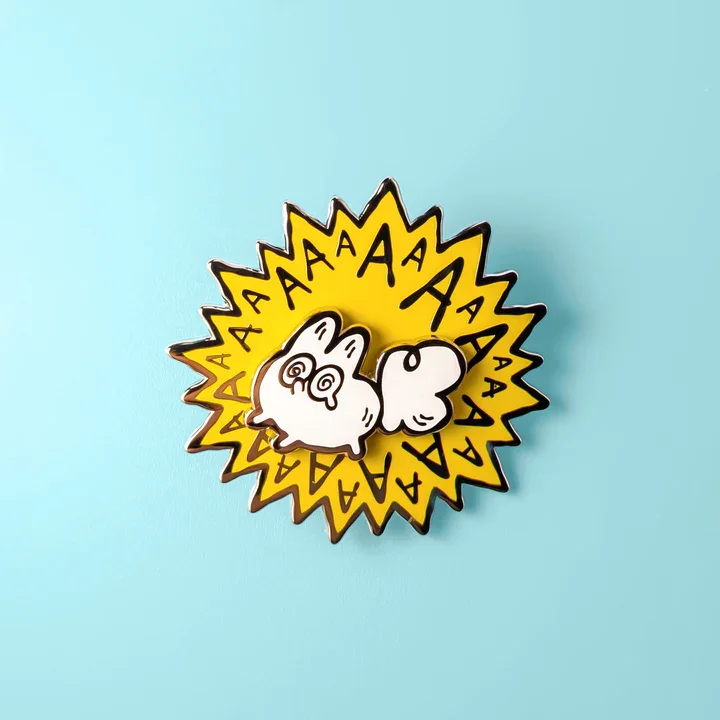 A colorful enamel pin featuring a white, cartoonish bunny with spiral eyes, surrounded by a yellow burst with black 'A's.