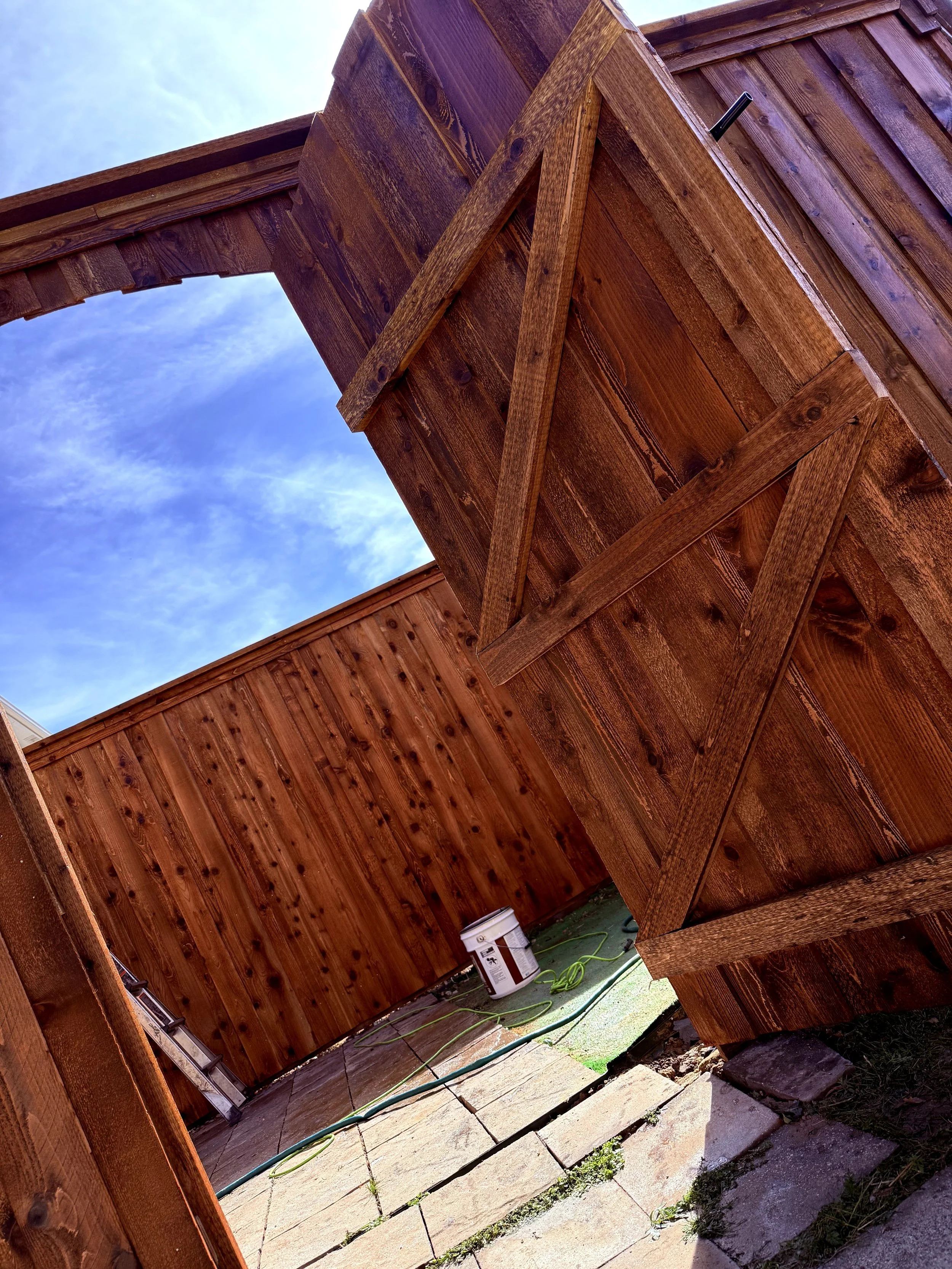 View of a wooden structure, possibly a deck or fencing, under construction with visible wooden planks and beams. The photo is taken from below, showing part of the sky with some clouds.