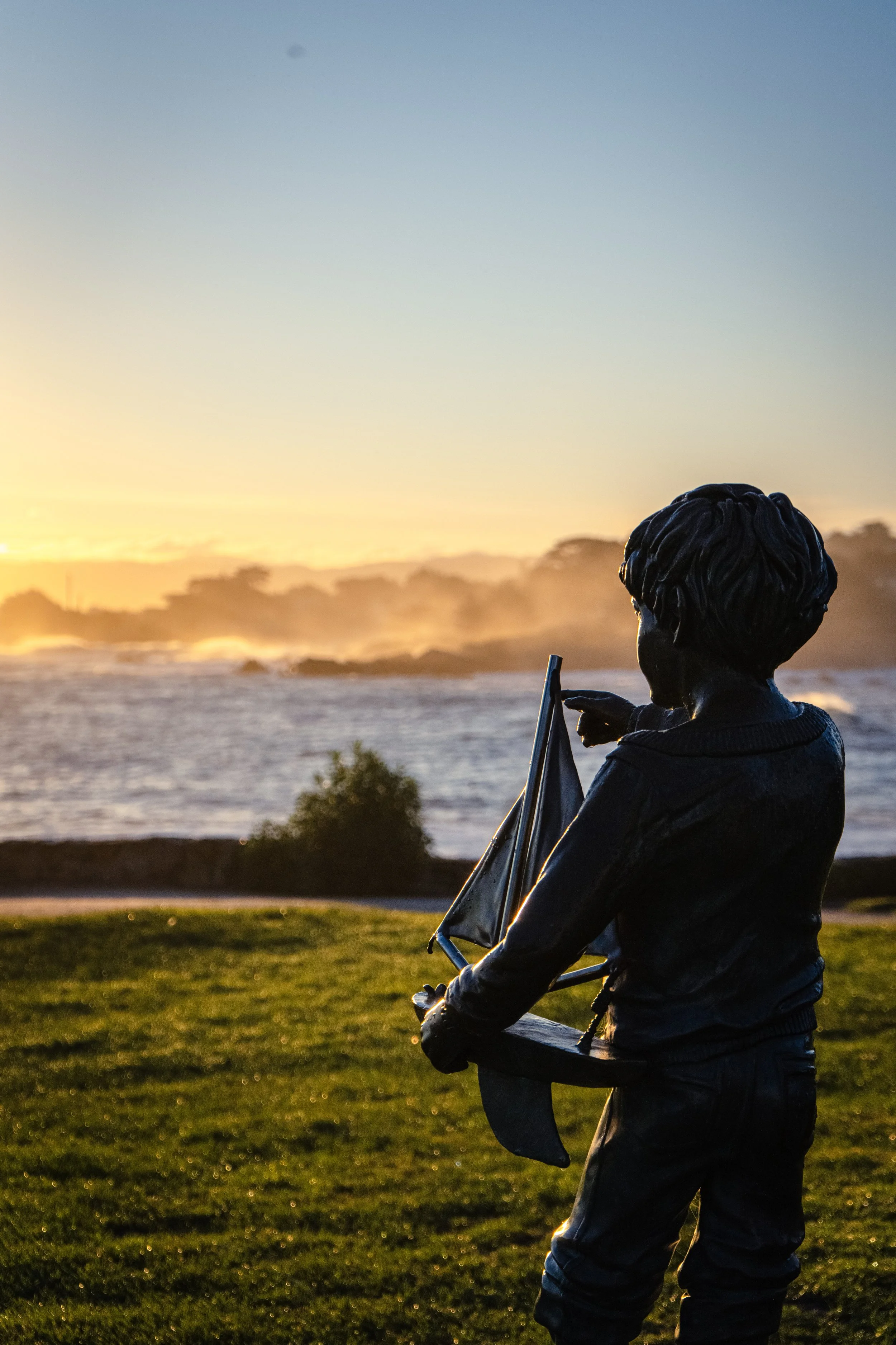 Statue at Lovers Point located in Pacific Grove, Ca of small boy holding a toy boat pointing out towards the Monterey Bay.