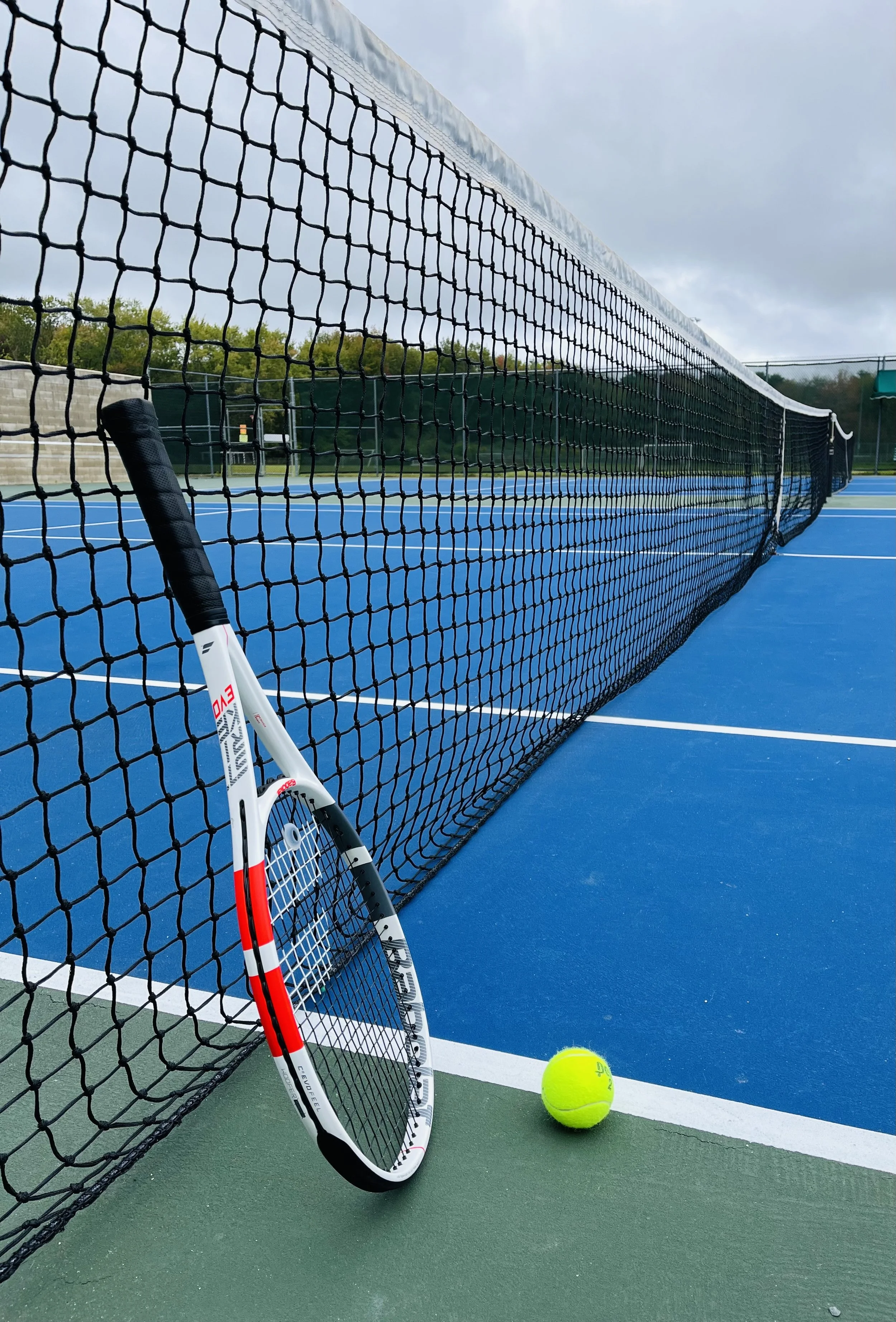 A tennis court with a tennis racket leaning against the net and a tennis ball on the ground near the court's edge.