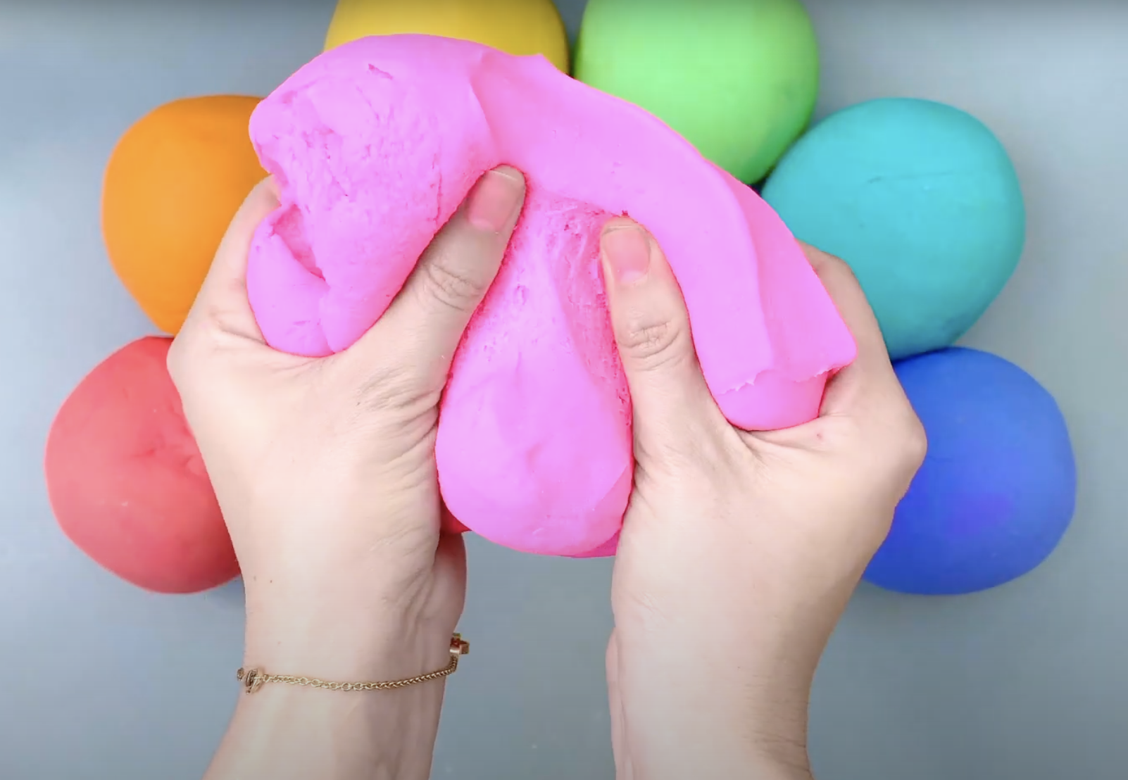 Person holding pink slime with multiple colorful slime balls in the background.