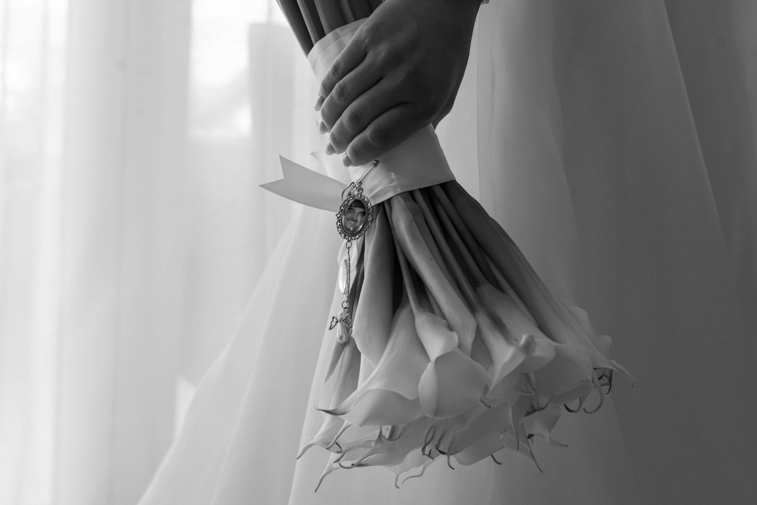 A person holding a bouquet of calla lilies, with a small photo charm attached to the ribbon around the bouquet.