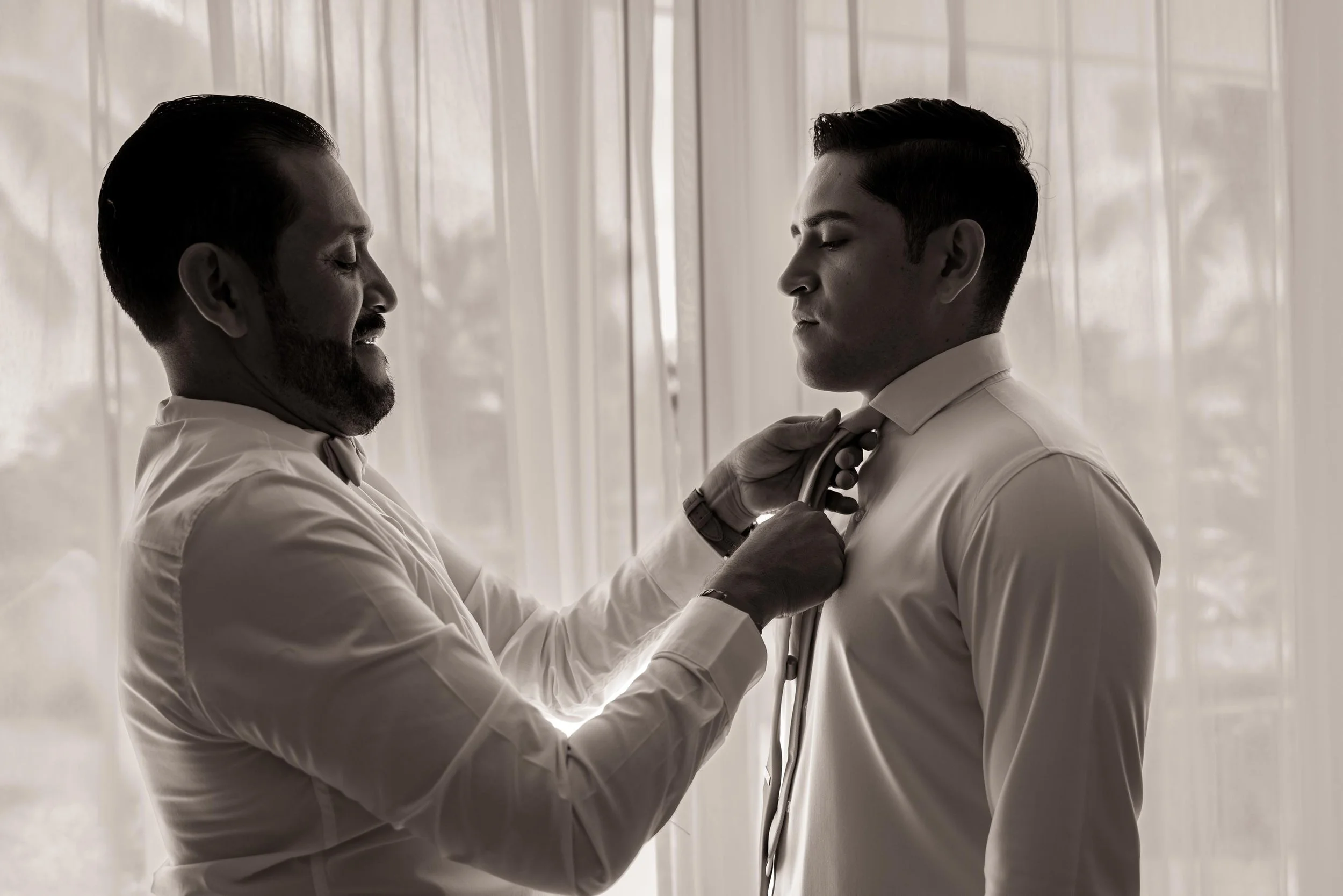 A doctor is helping a young man prepare for a formal event, adjusting his tie's knot.