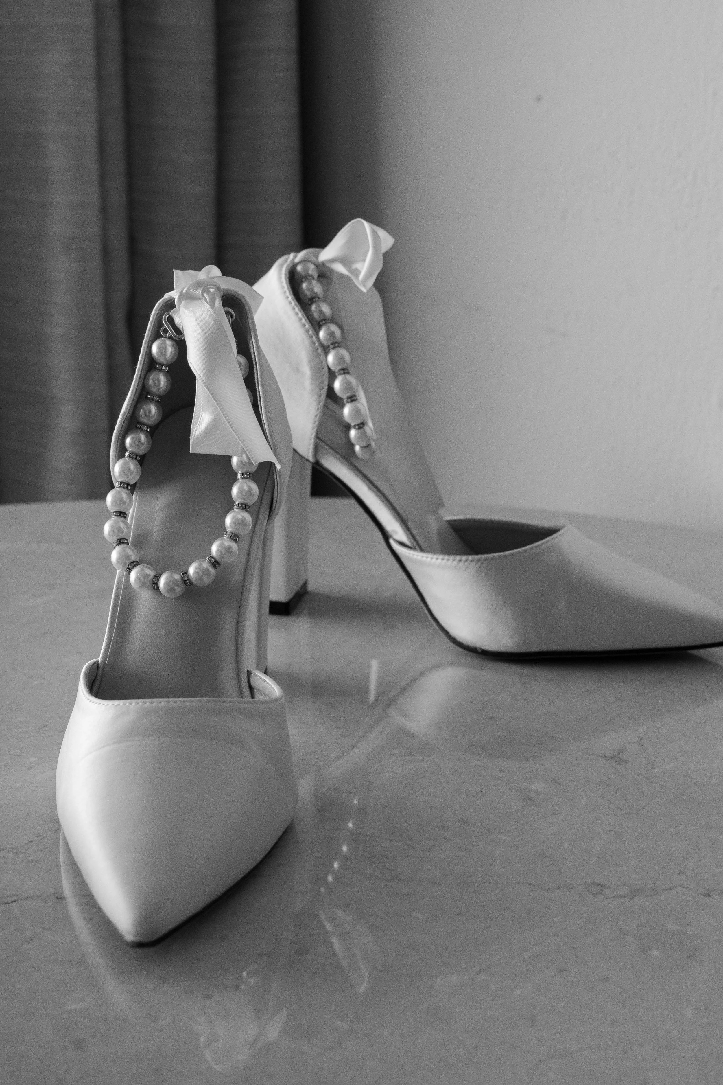 White high-heeled shoes with pearl strap accessories on a polished surface.