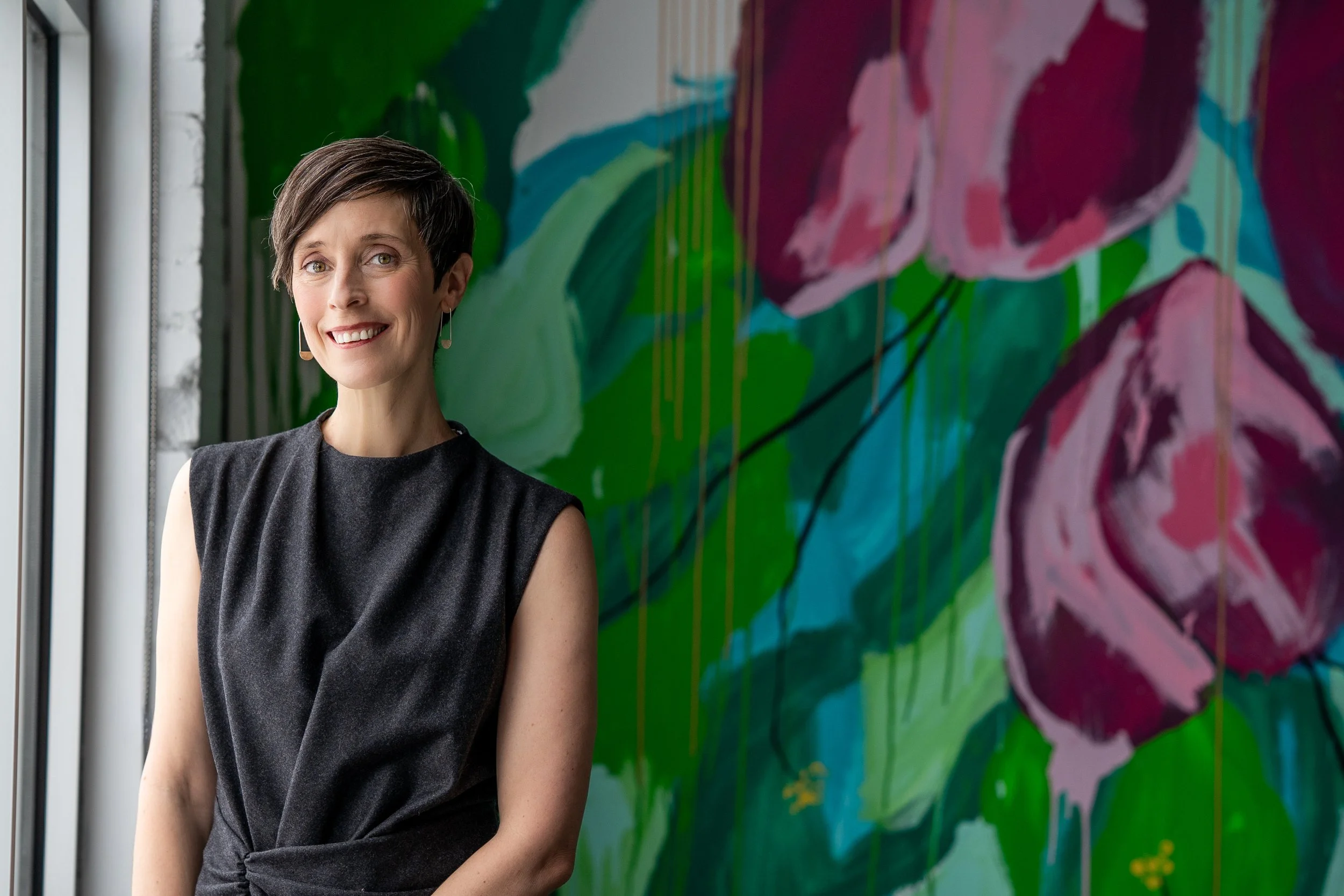Dr. Brown stands at a window with a green leafy mural behind her. For people seeking combined medication and psychotherapy treatment, you can get both here.