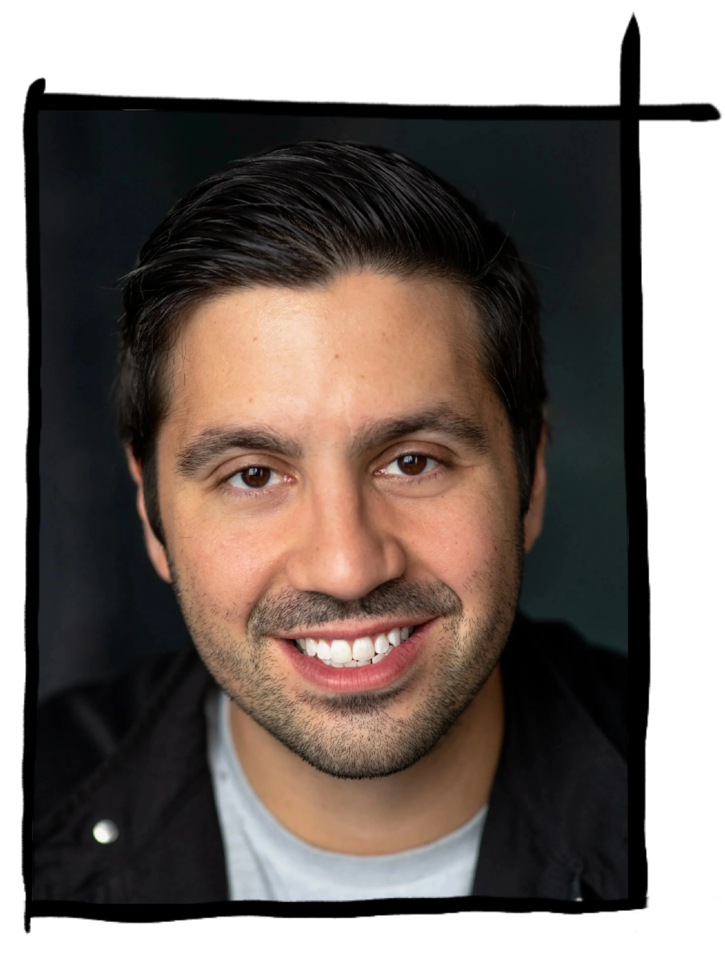 A close-up portrait of a smiling man with dark, slicked-back hair and light stubble, wearing a dark jacket and gray shirt against a dark background.