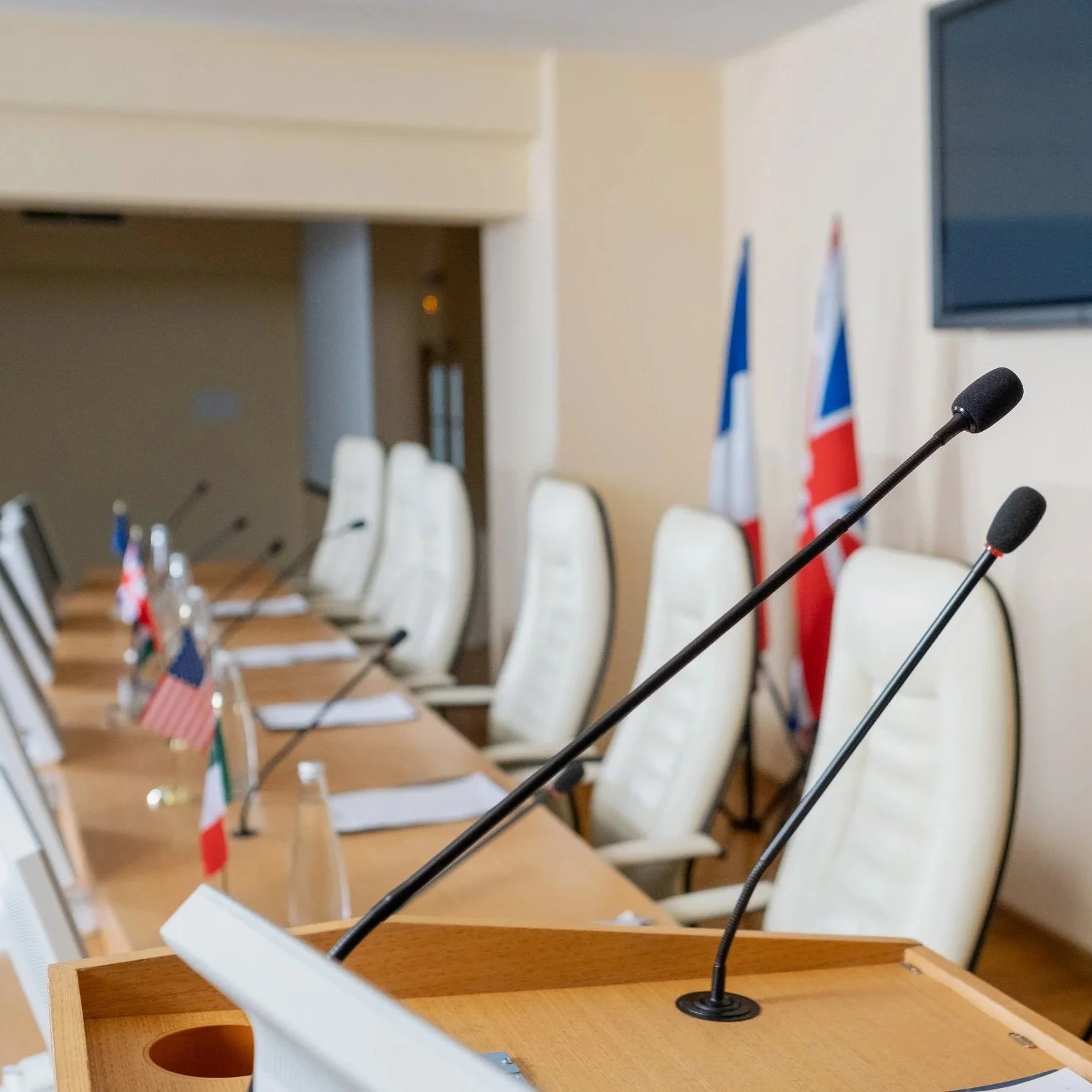 Salle de conférence avec des microphones, des drapeaux et des chaises blanches alignées.