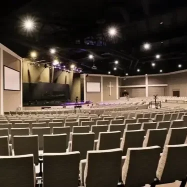 Intérieur d'une salle de congrès ou d'église avec de nombreuses chaises, un grand écran, une croix et un podium.