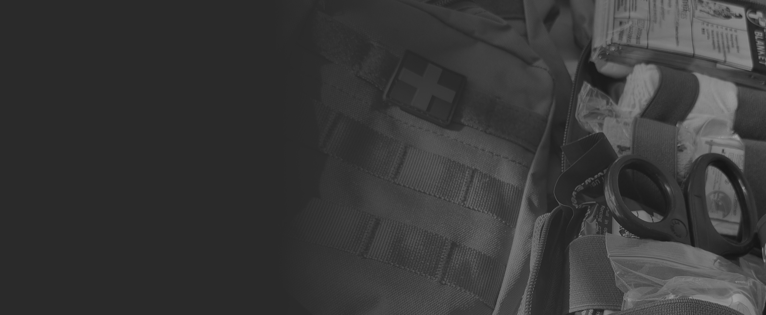 Close-up of a tactical vest with various equipment attached, including a rescue tool, a plastic bag, and a medical patch.
