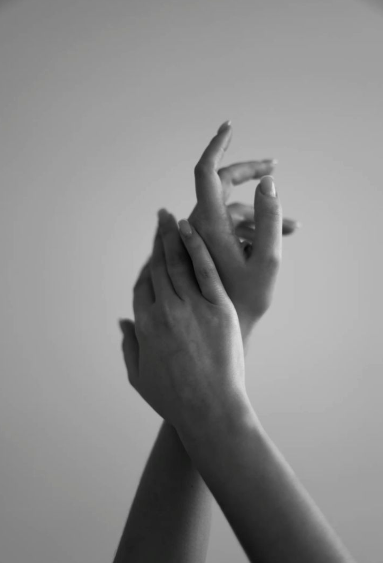 Black and white photo of two hands softly touching, with one hand gently holding the other, against a plain background.