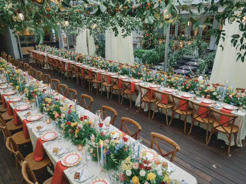 Long banquet tables set for a wedding or event, decorated with colorful floral centerpieces, candles, and tableware at Mattie's.