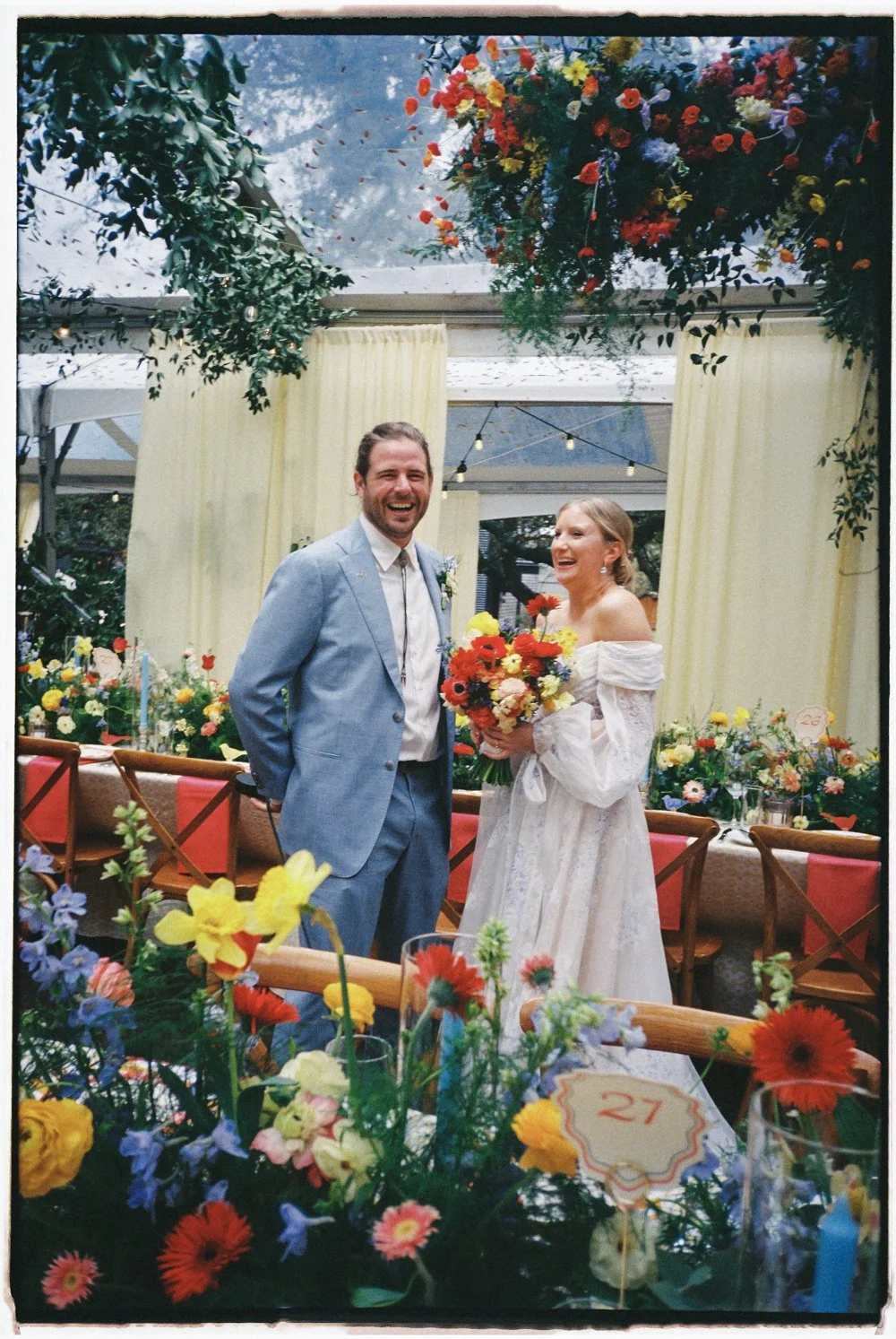 A bride and groom smiling at a wedding reception with colorful flowers and decorations.