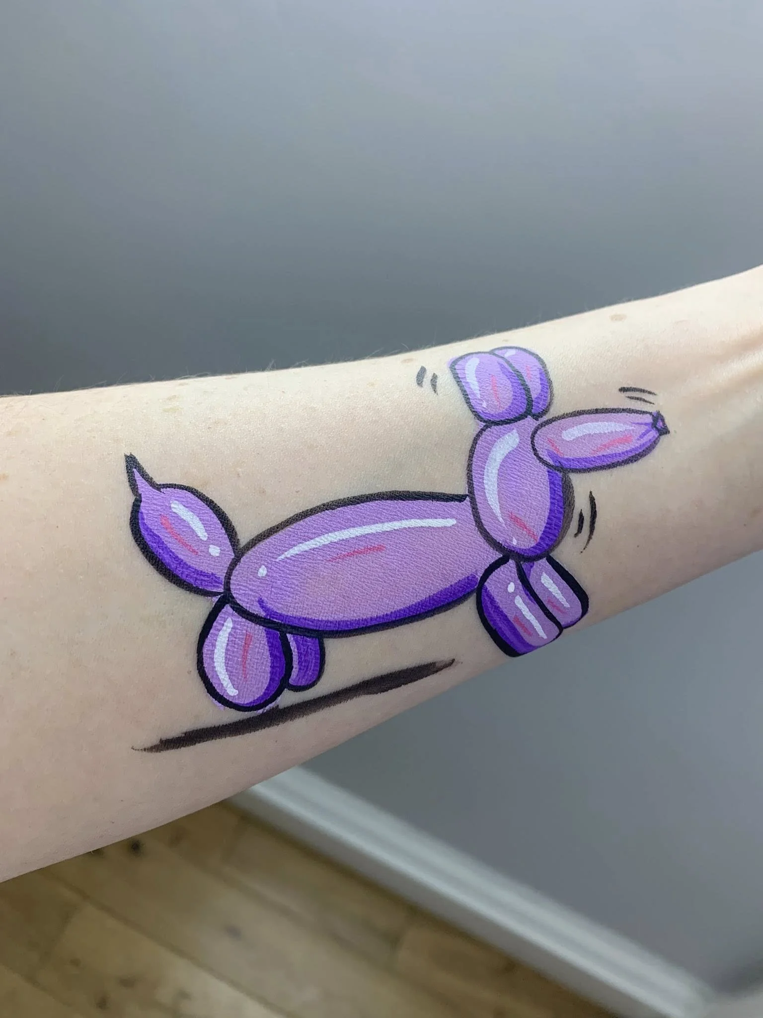 Face paint on arm of Jeff Koons balloon dog. Purple with shading, dog depicted in a wagging tail pose.