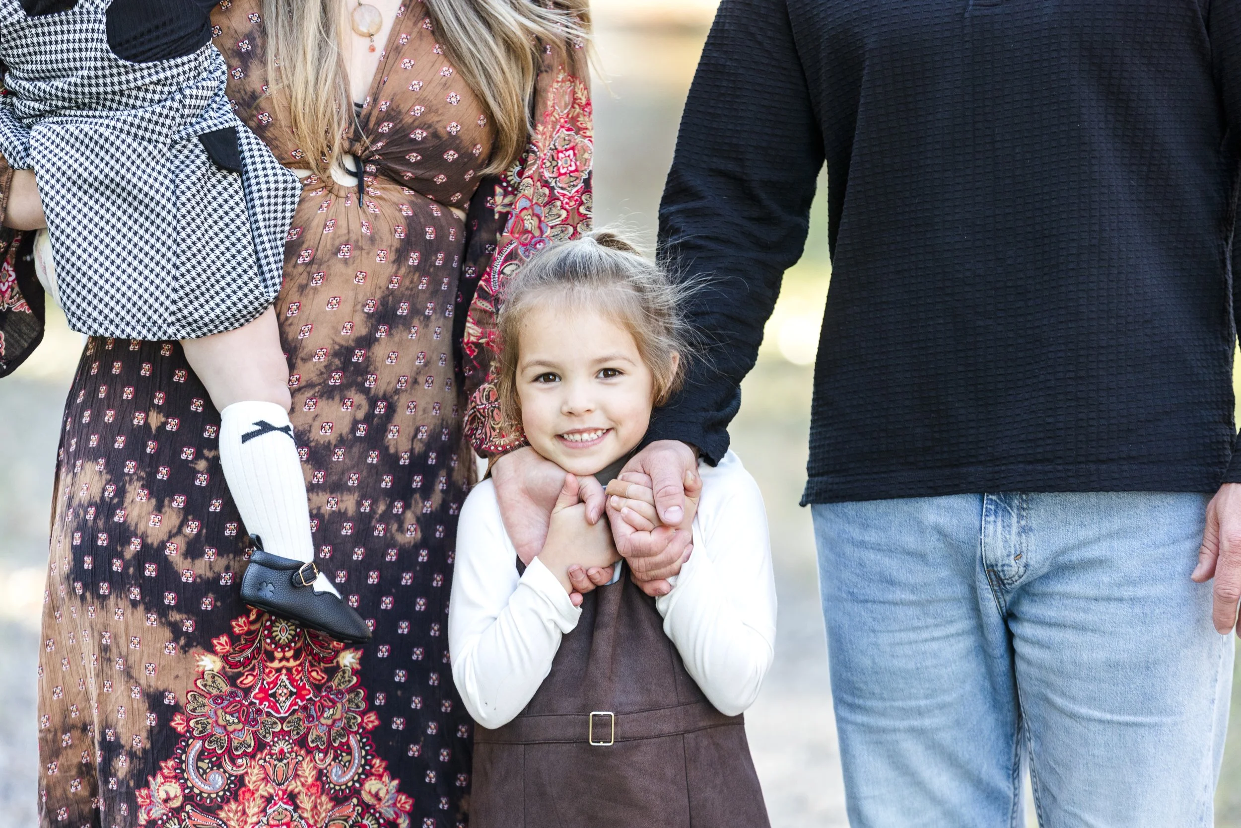Young girl with long hair smiling, being held by an adult, surrounded by family members outside.