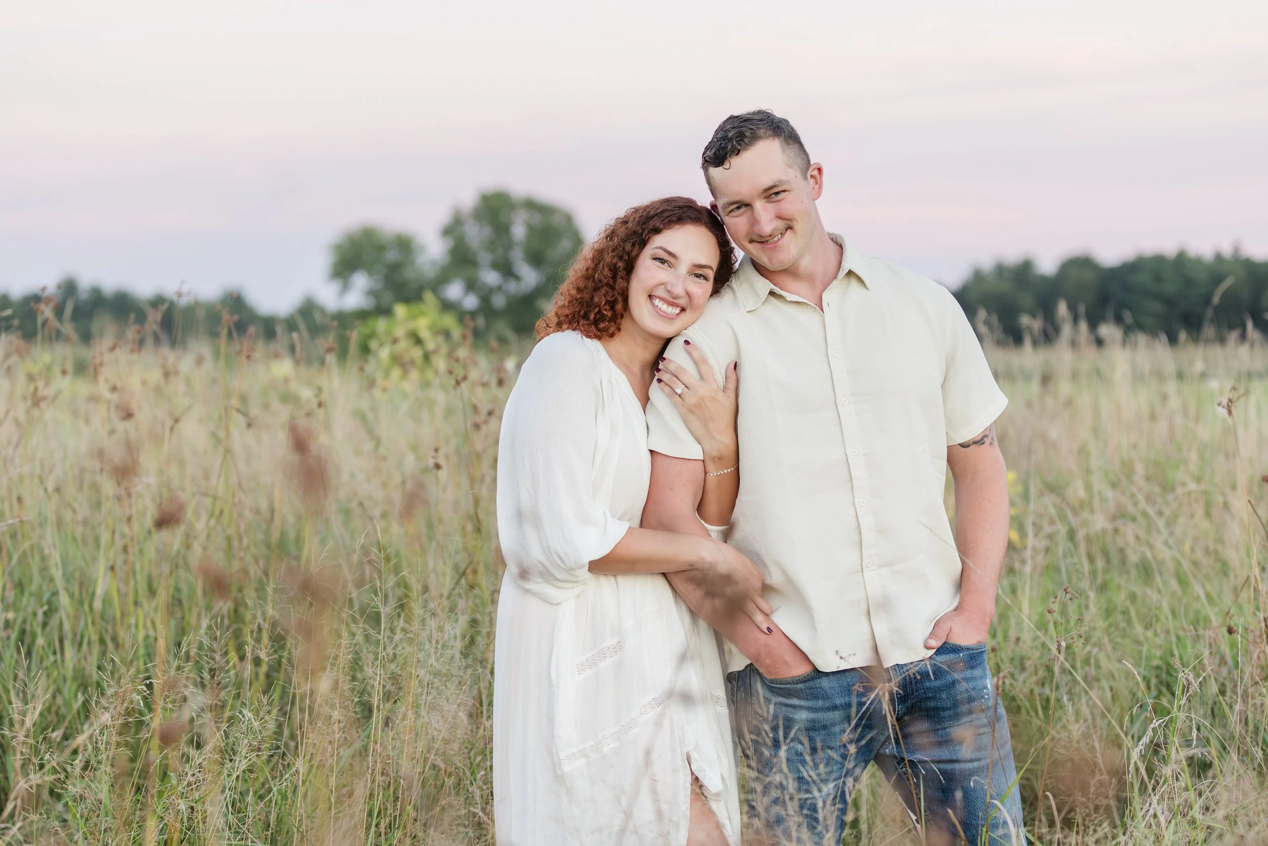 Couple standing in a field at sunset, smiling and embracing